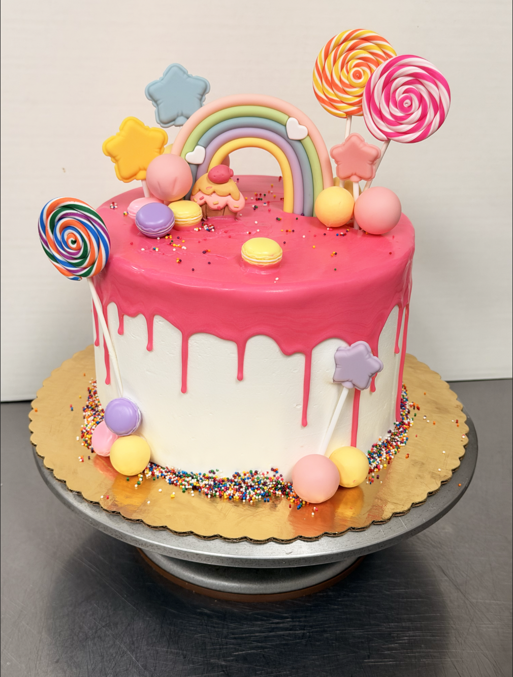 Gluten Free Cake with pink dripping icing decorated with colorful candies, lollipops, stars, and a rainbow topper.