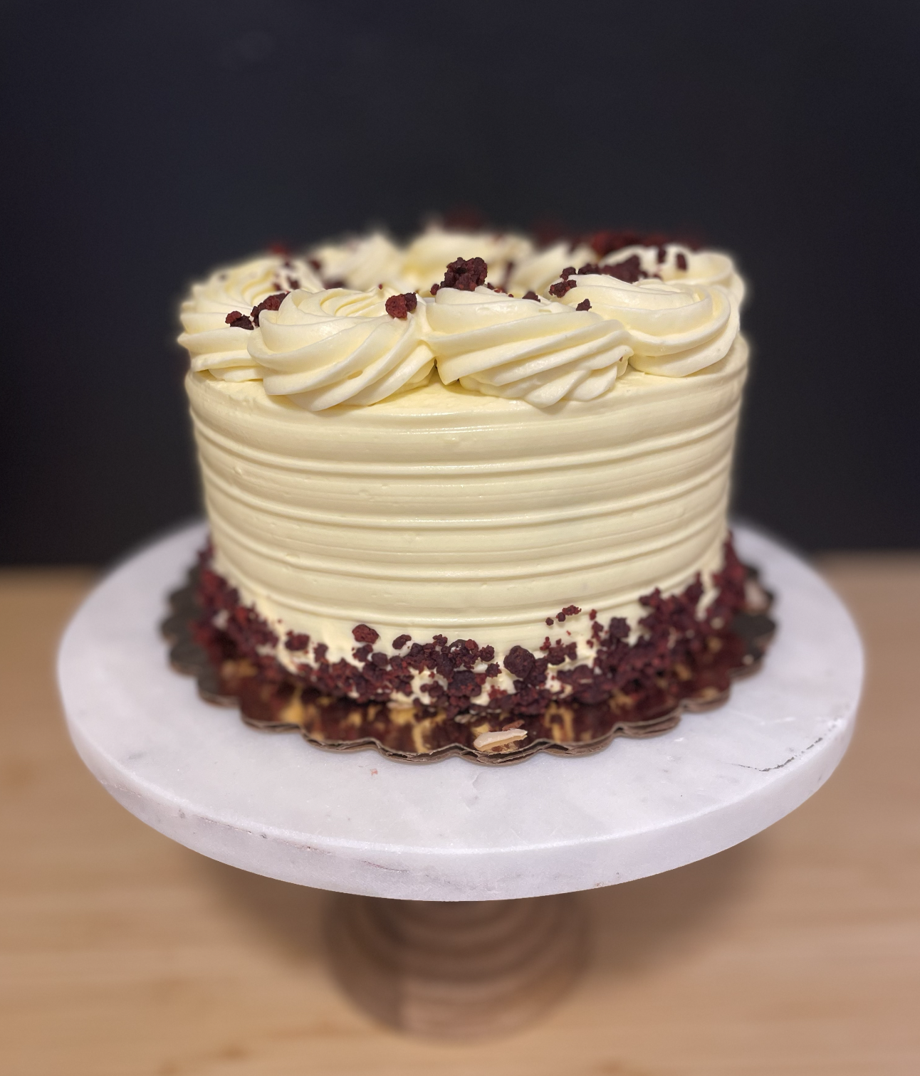 Gluten Free round white frosted cake decorated with piped white frosting and red crumbles on top, placed on a white cake stand.