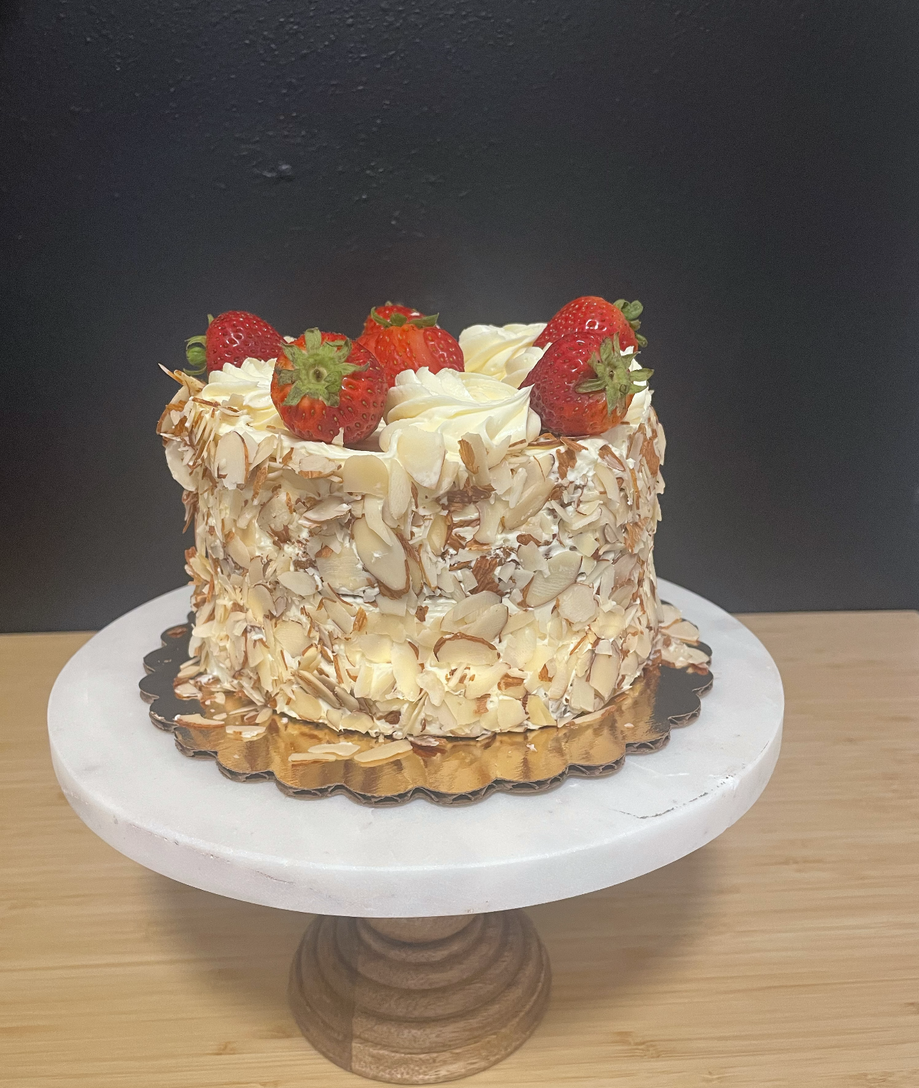 Gluten Free round cake decorated with fresh strawberries and almond slices on a white marble stand.