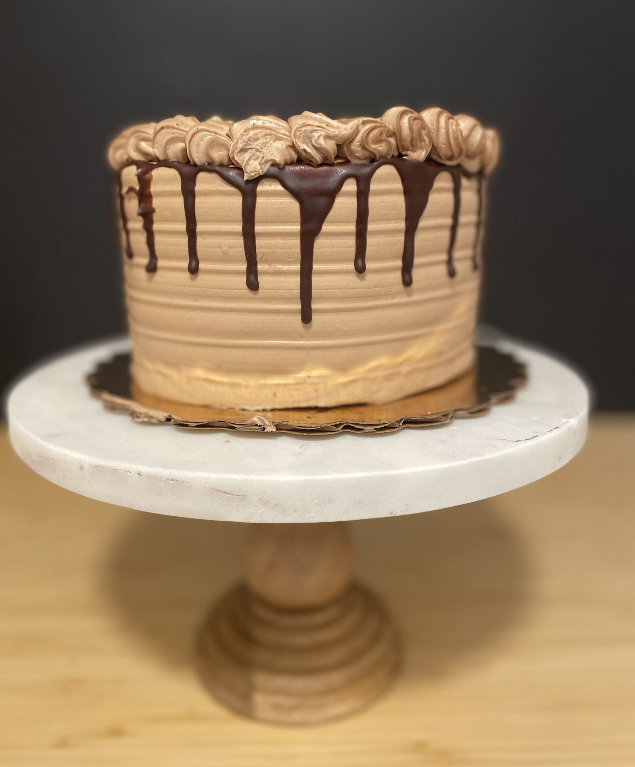 Gluten Free Cakes Chocolate and caramel cake with chocolate drip decoration and piped frosting on top, displayed on a white cake stand.