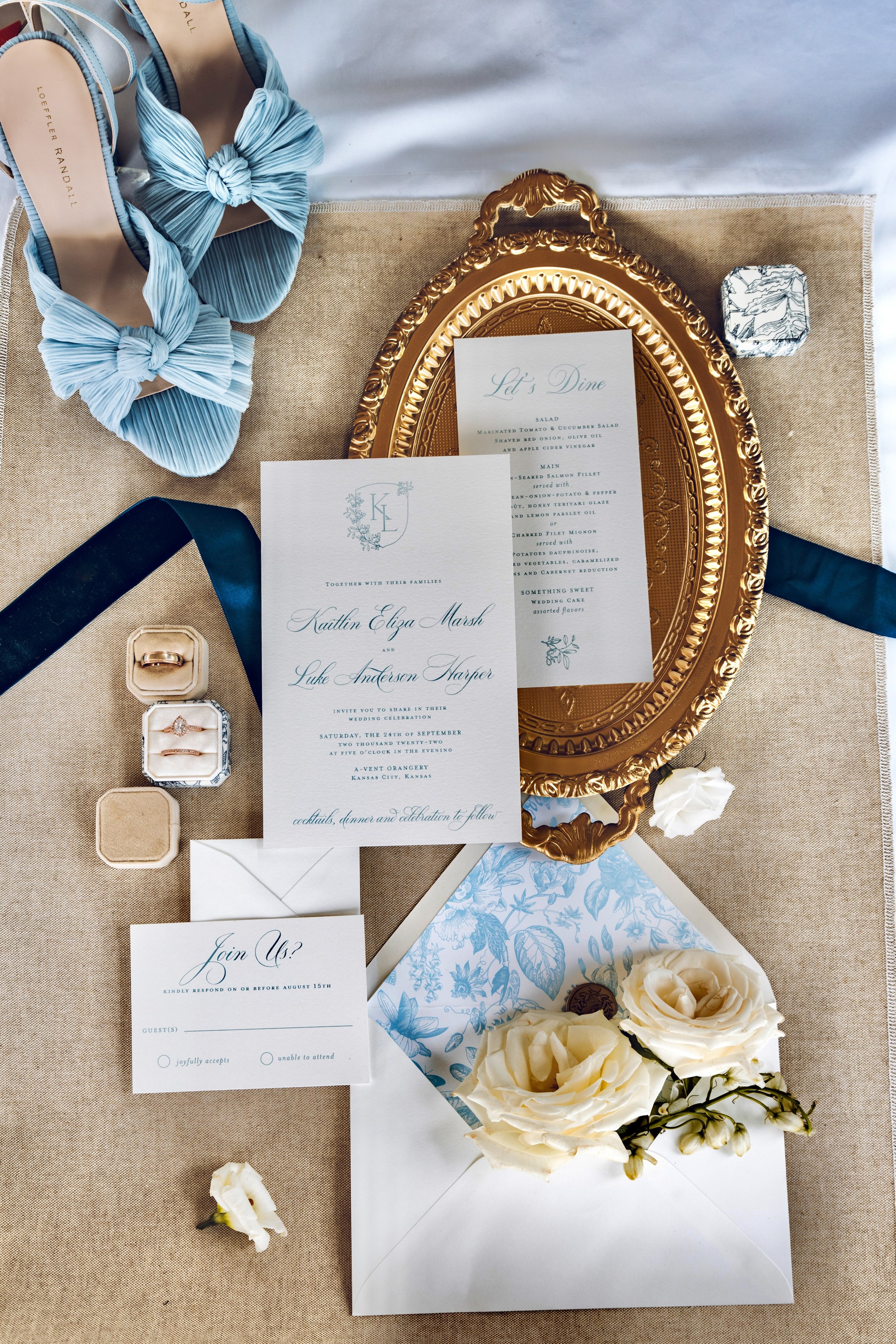 Wedding invitation suite with RSVP card, wedding menu, floral arrangements, shoes, and jewelry displayed on a beige table. Photographed by the talented Keri-ann Gordon