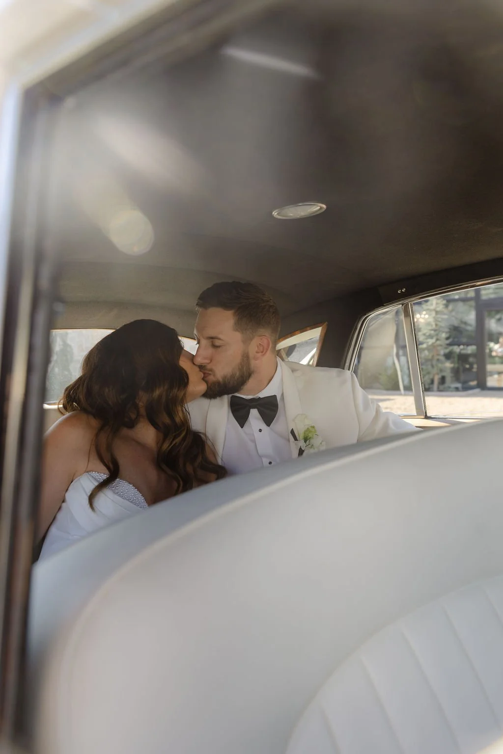 A bride and groom sharing a kiss in the backseat of a vintage car, with the bride in a white wedding dress and the groom in a tuxedo, taken by KA Gordon Photography based in Kansas and worldwide