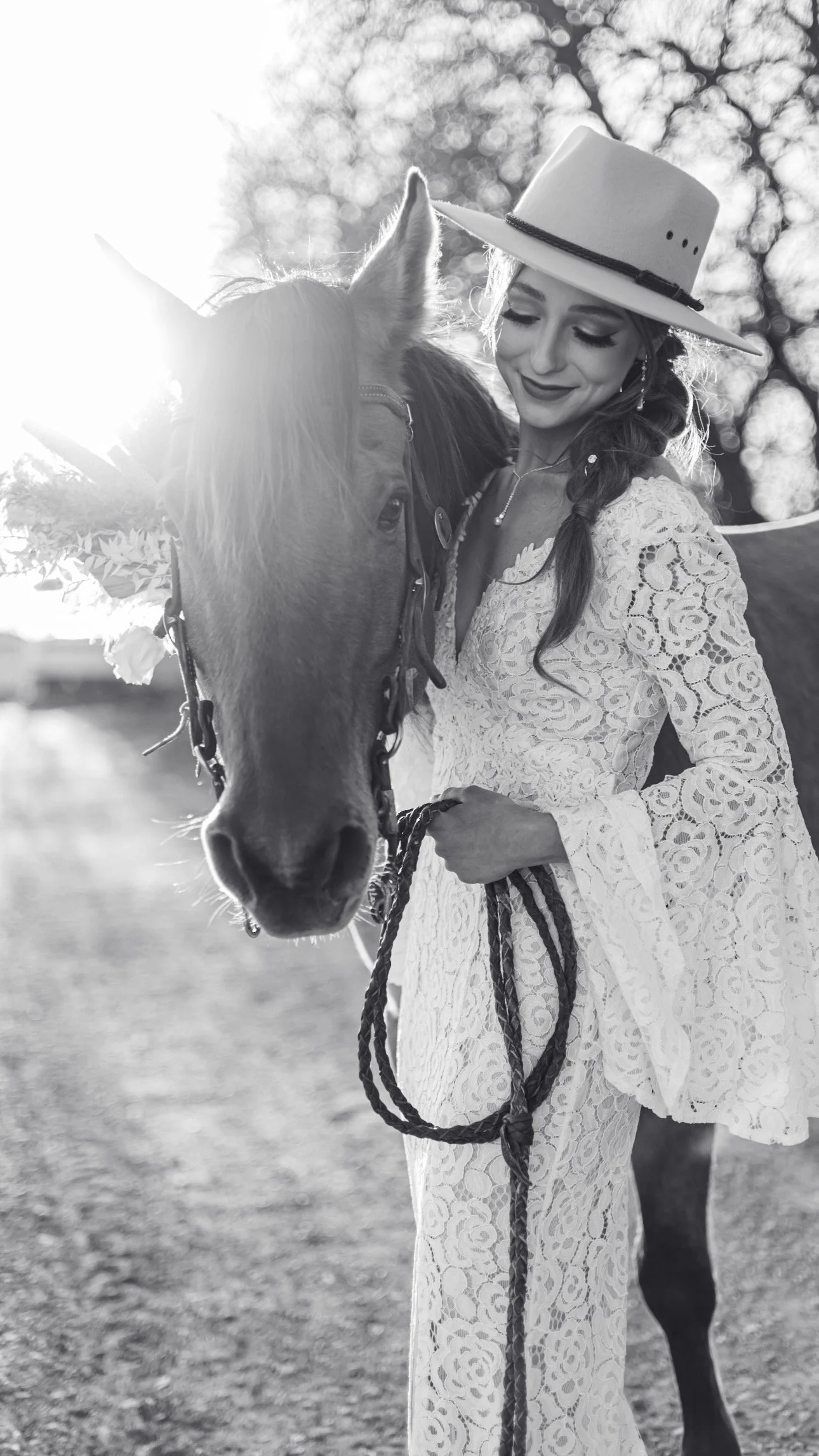 Black and white photo of a woman in a lace dress and wide-brimmed hat standing next to a horse, holding its reins. Kansas premier equine photographer