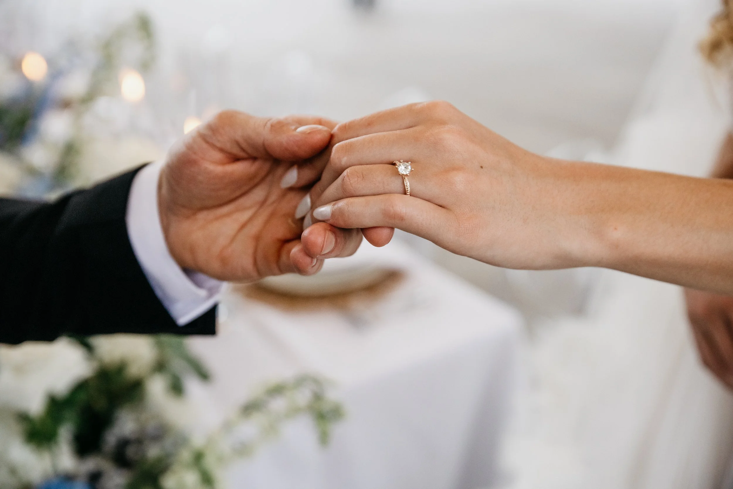 Close-up of a bride and groom holding hands, with the bride wearing an engagement ring with a large diamond. Kansas luxury wedding photographer