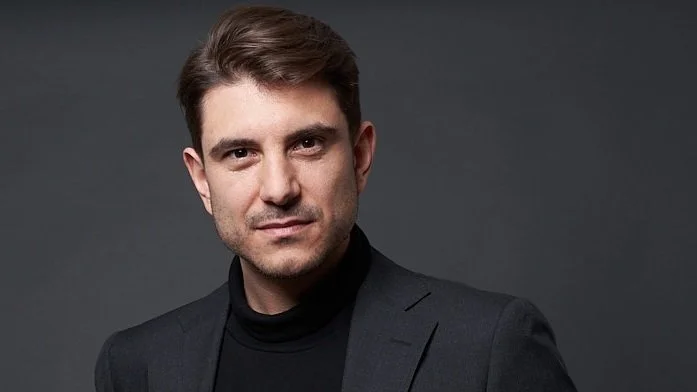 Porträt eines Mannes, der schwarze Jacke und schwarzen Rollkragen trägt, dunkler grauer Hintergrund