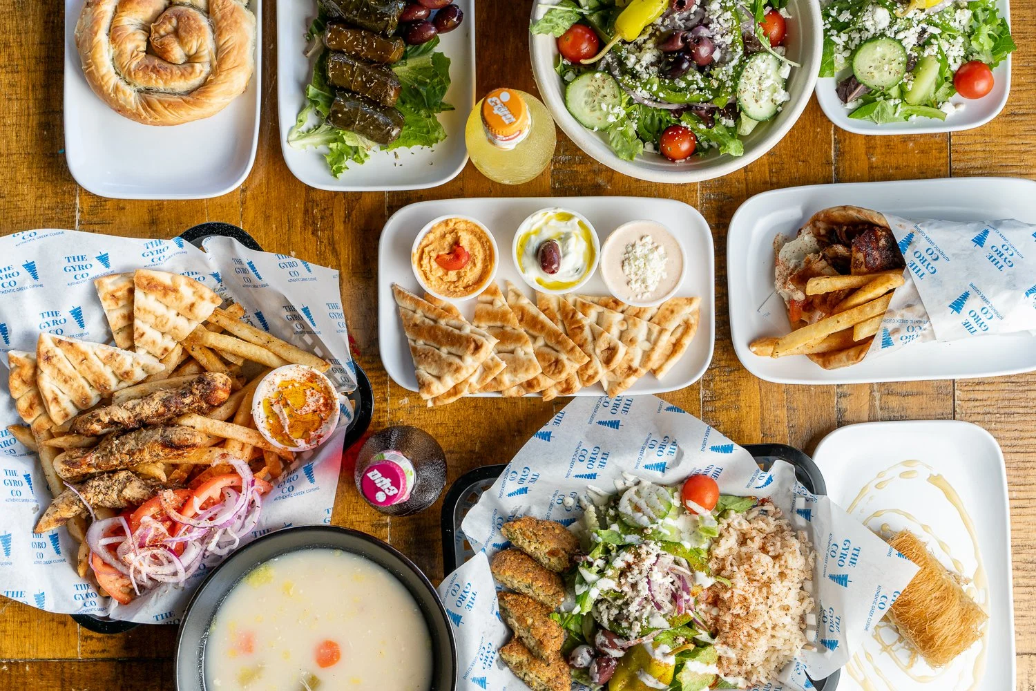 Assorted Middle Eastern dishes including salads, pita bread, grilled fish with fries, hummus, baba ganoush, and desserts on a wooden table.
