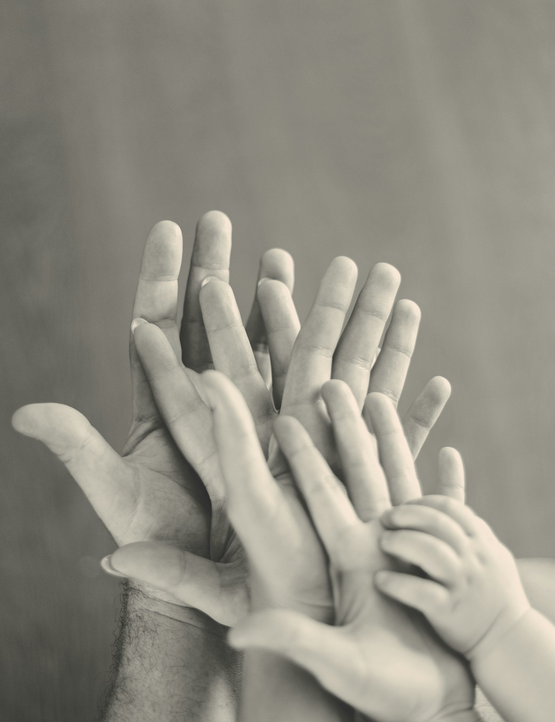 Multiple hands, including a child's hand, stacked together against a plain background.