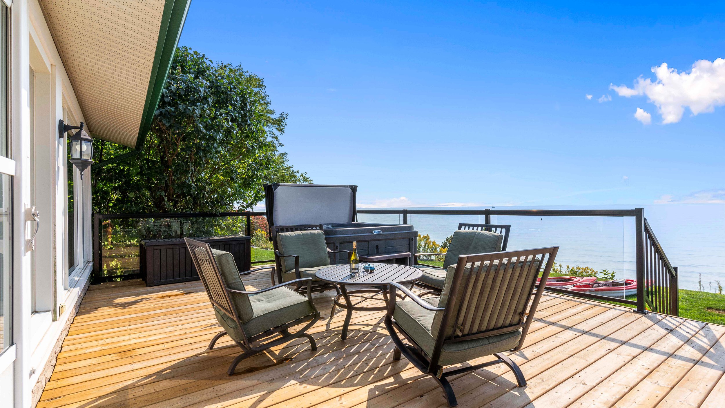 Outdoor patio with seating, table, and hot tub on wooden deck overlooking a lake.