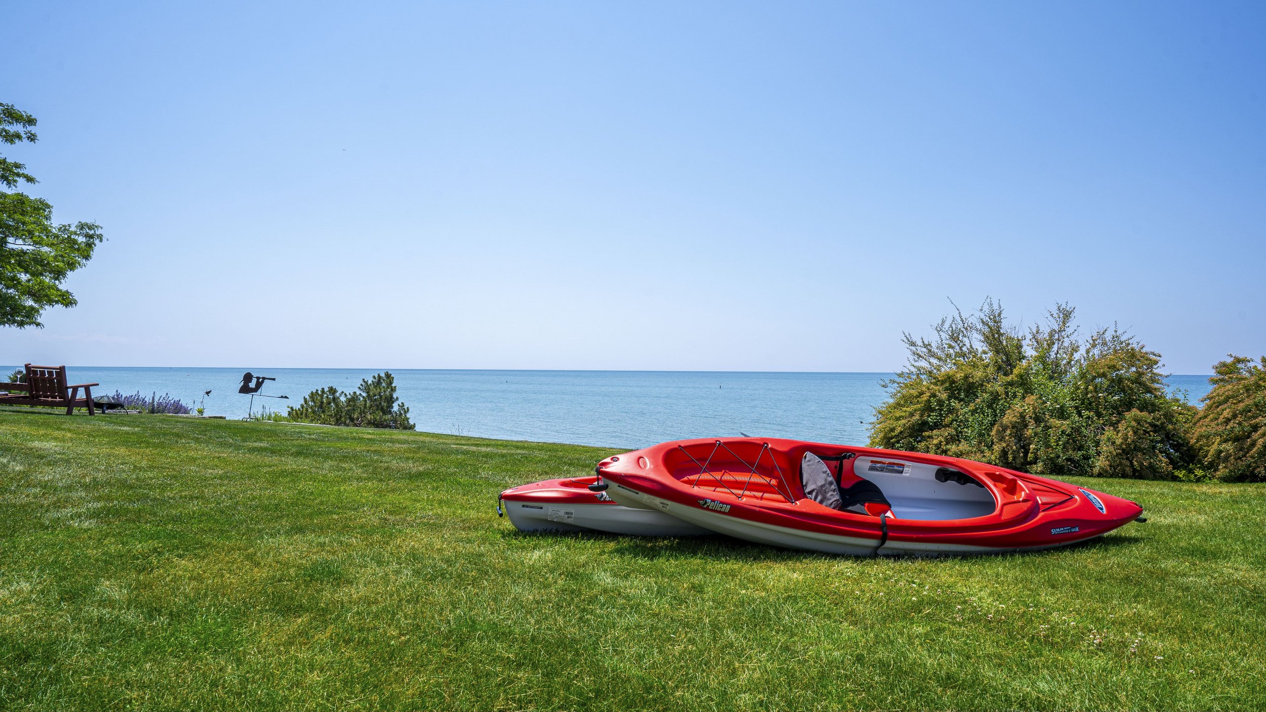 Two red kayaks on green grass with a lake and trees in the background.