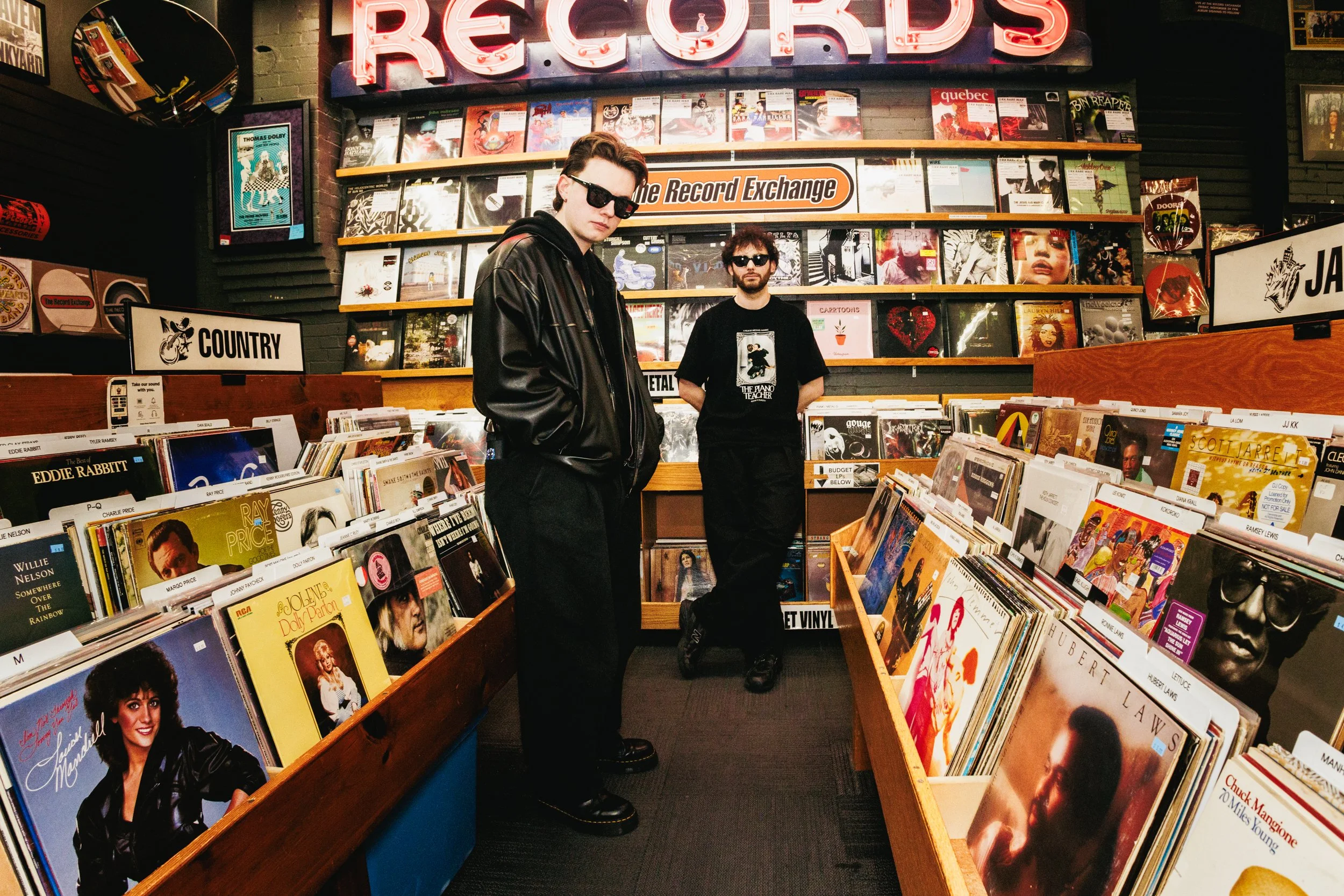 Two young men with dark sunglasses and black outfits shopping for vinyl records at a record store named R.E.C.O.R.D.S.
