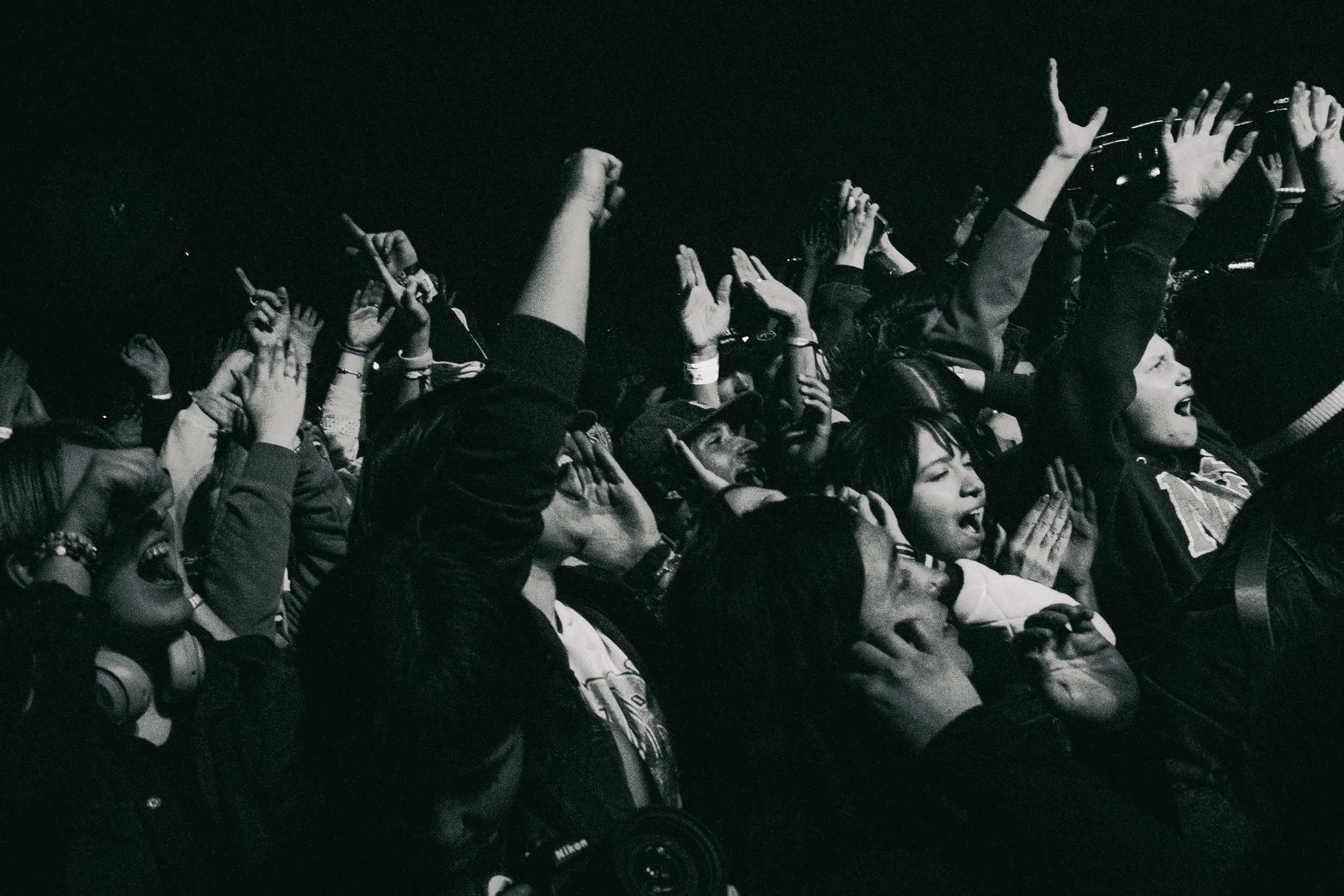 A crowd of people at a concert or event, cheering, raising hands, and enjoying the moment, with some wearing headphones and others with expressions of excitement and joy.