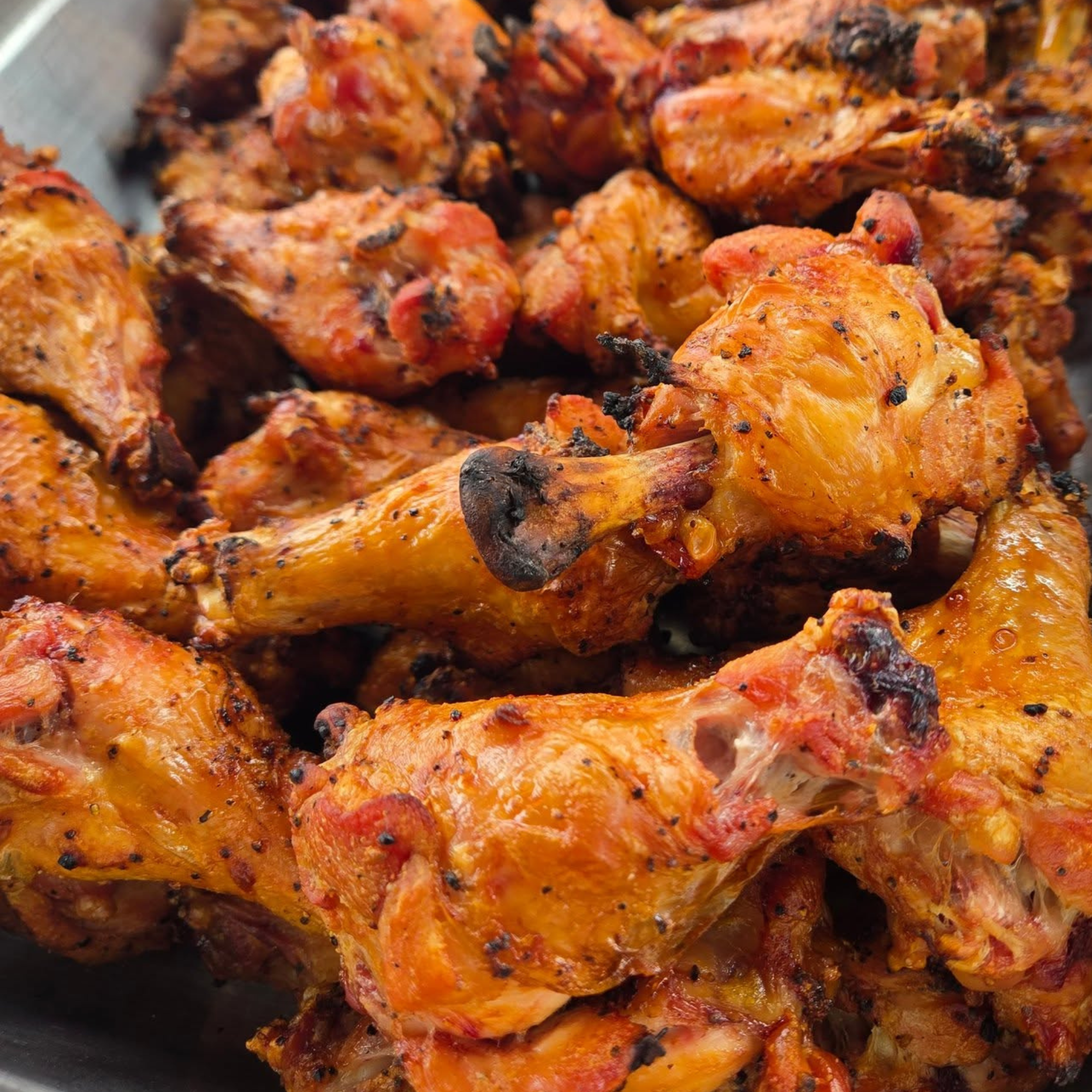 Close-up of grilled chicken pieces covered in orange marinade and black pepper.