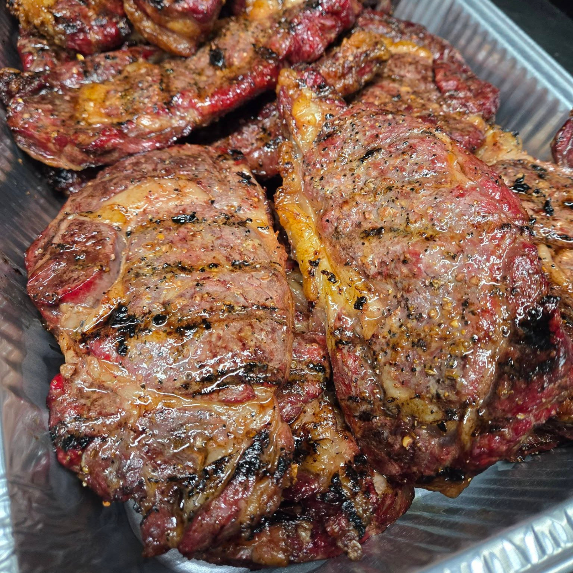 Close-up of grilled steak pieces with seasoned surface in a metal pan.