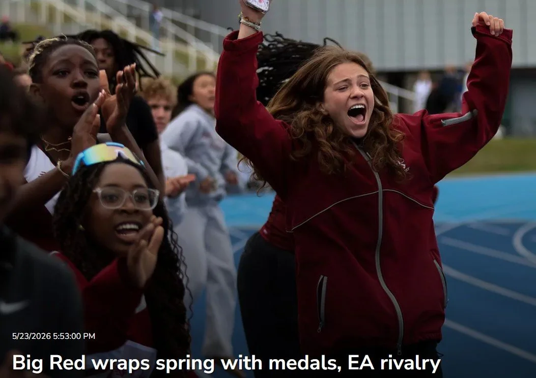 Young woman with curly hair in a red jacket celebrating with others on a track field