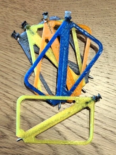 A collection of colorful bicycle brake calipers in yellow, blue, orange, and gray, arranged on a wooden surface.