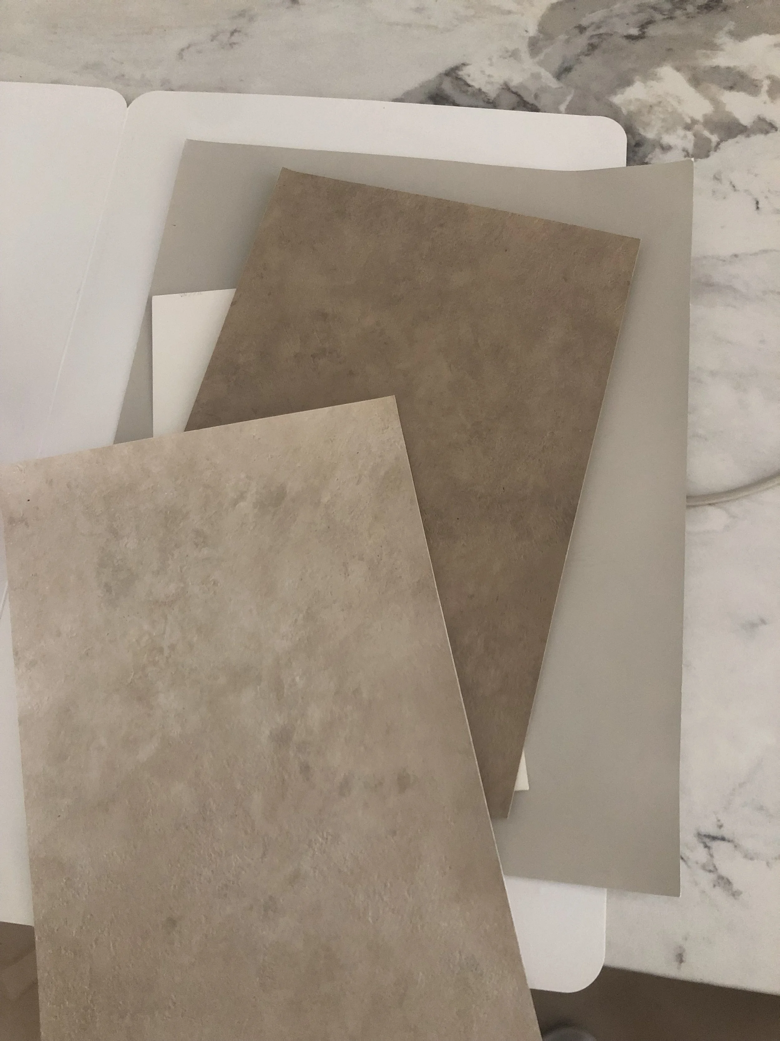 Samples of beige and brown textured plaster, lime wash, custom finishes on a white surface.