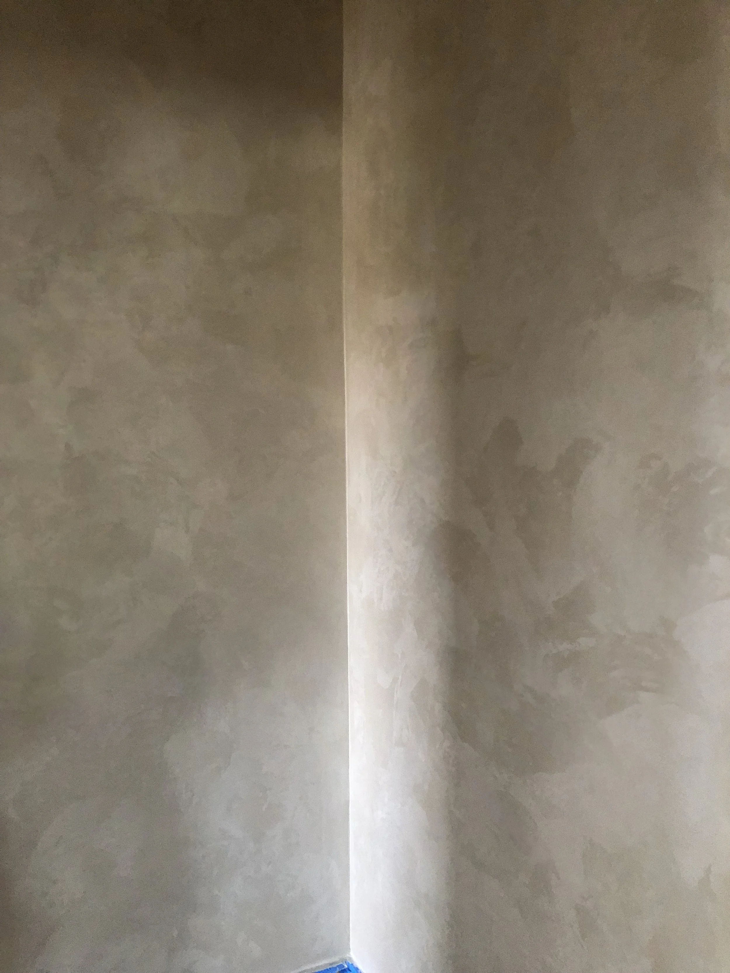 Two beige lime wash textured walls meeting at a corner, with a strip of light between them and a blue floor base at the bottom.
