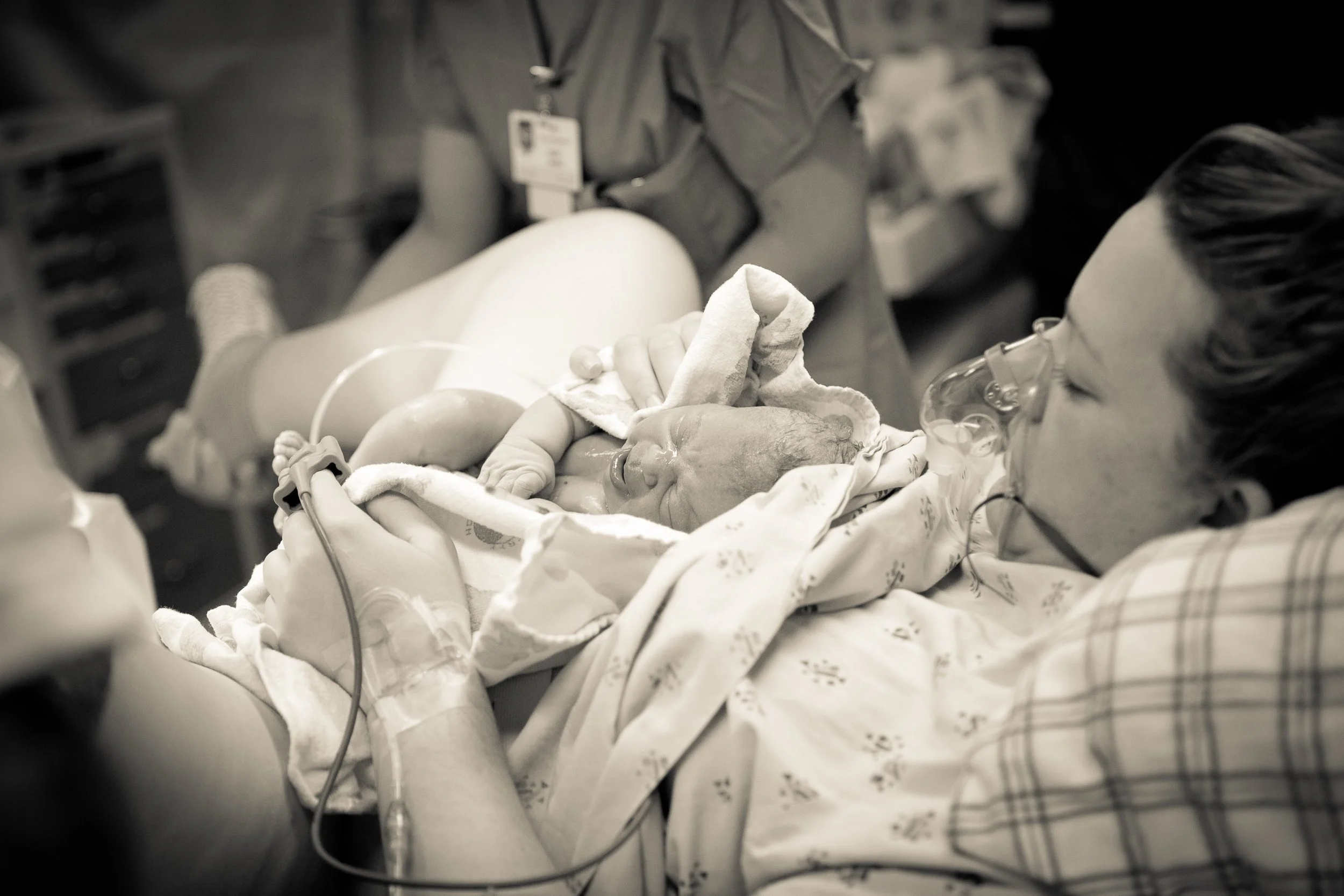 Baby in a hospital bassinet with medical equipment nearby, held by a woman.