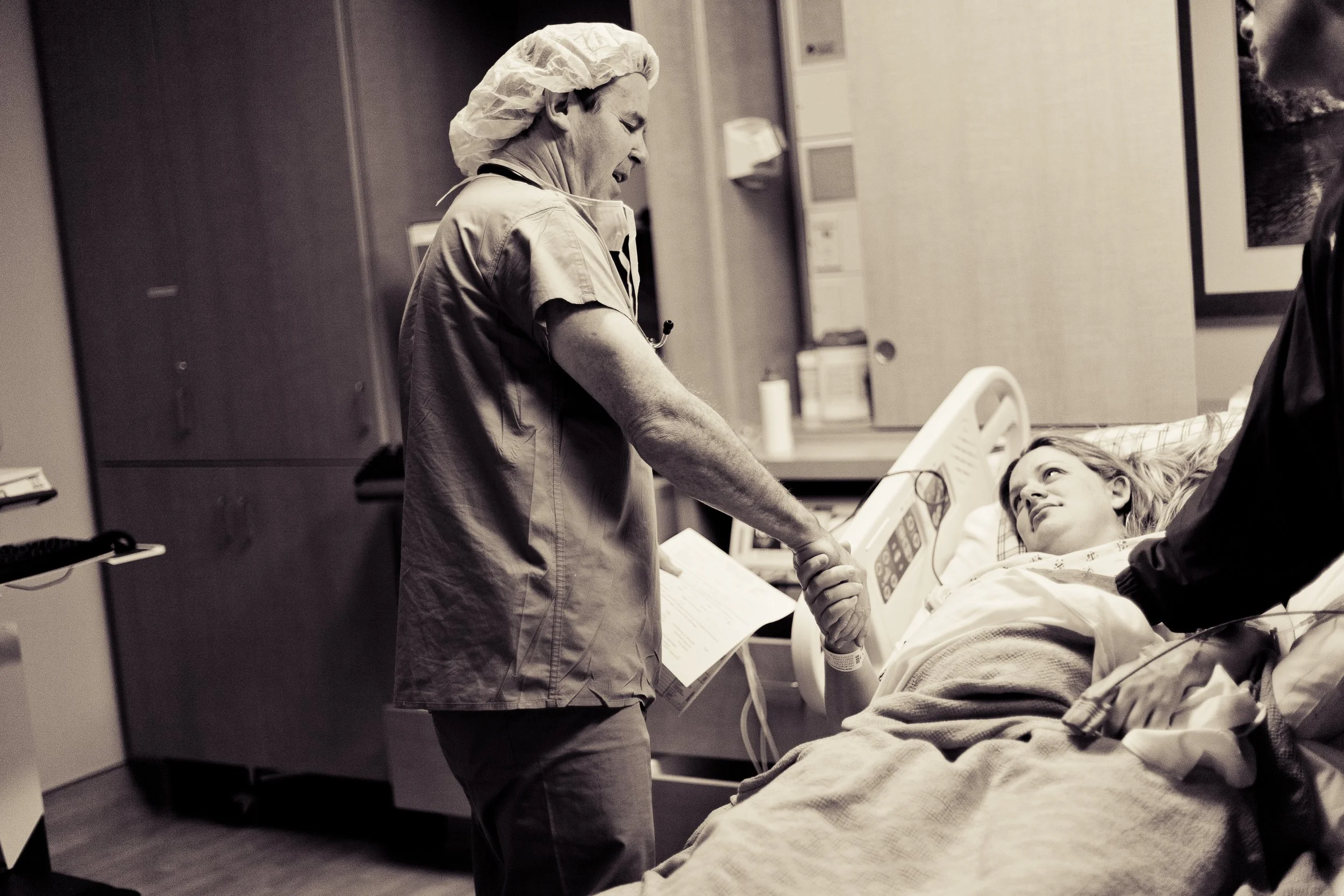 A healthcare worker holding hands with a young patient in hospital bed, both smiling and sharing a moment of connection in a hospital room.