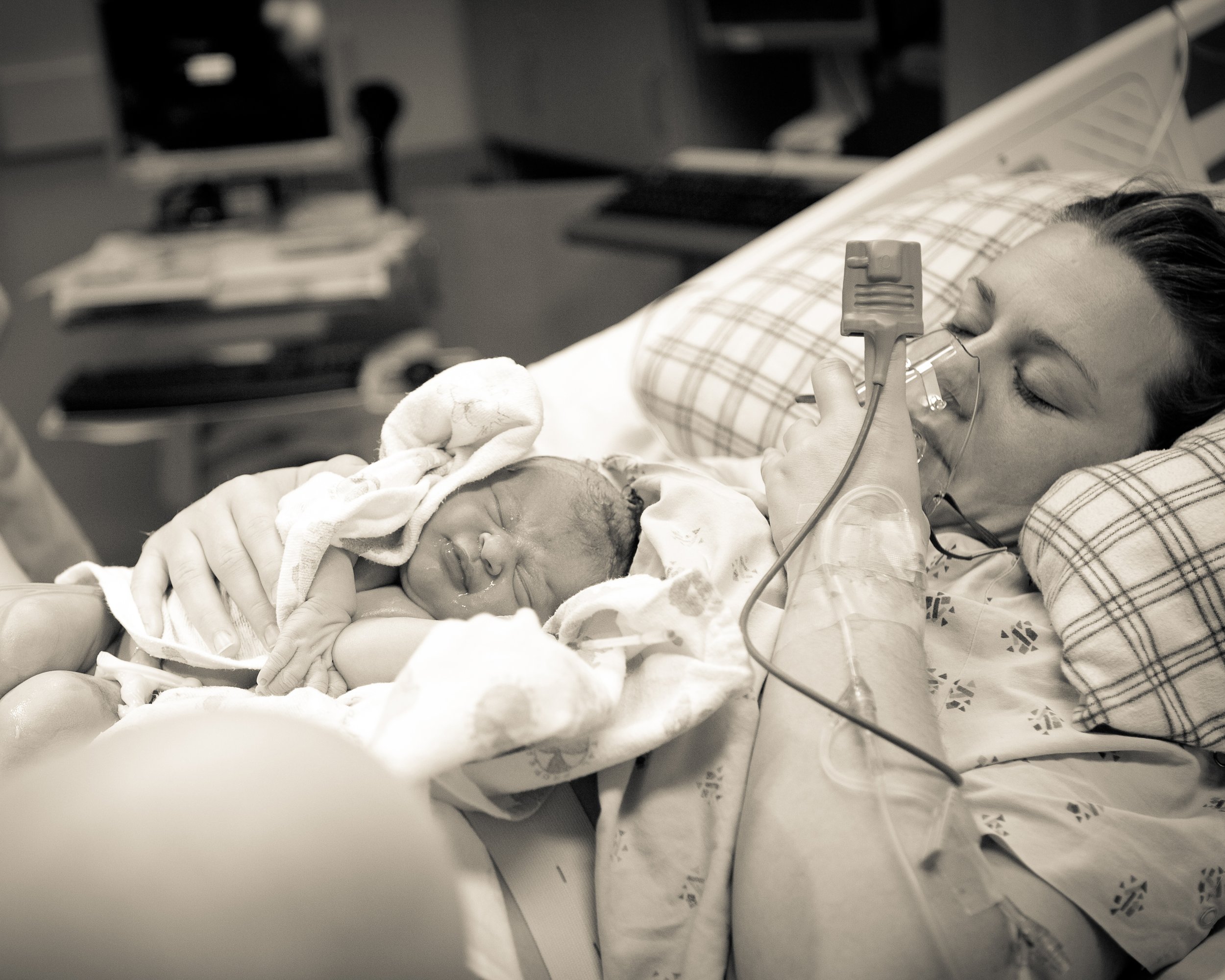 A person lying in a hospital bed with medical equipment, being given oxygen and monitored, suggesting they are in a healthcare setting.