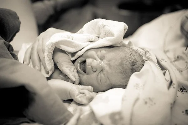 A newborn baby crying and being held by medical staff after birth.