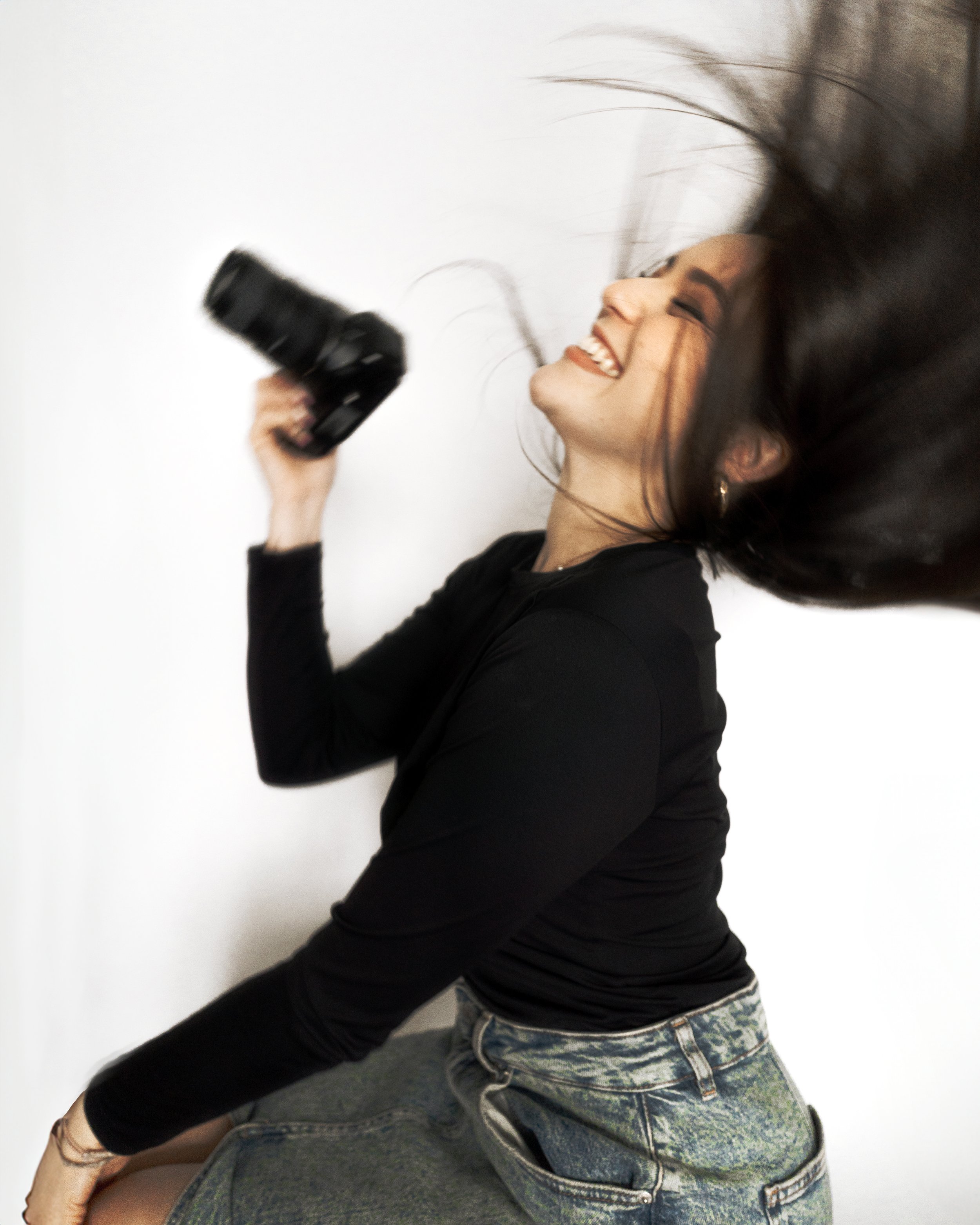 Personne souriante tenant un appareil photo, mouvement des cheveux, fond blanc.
