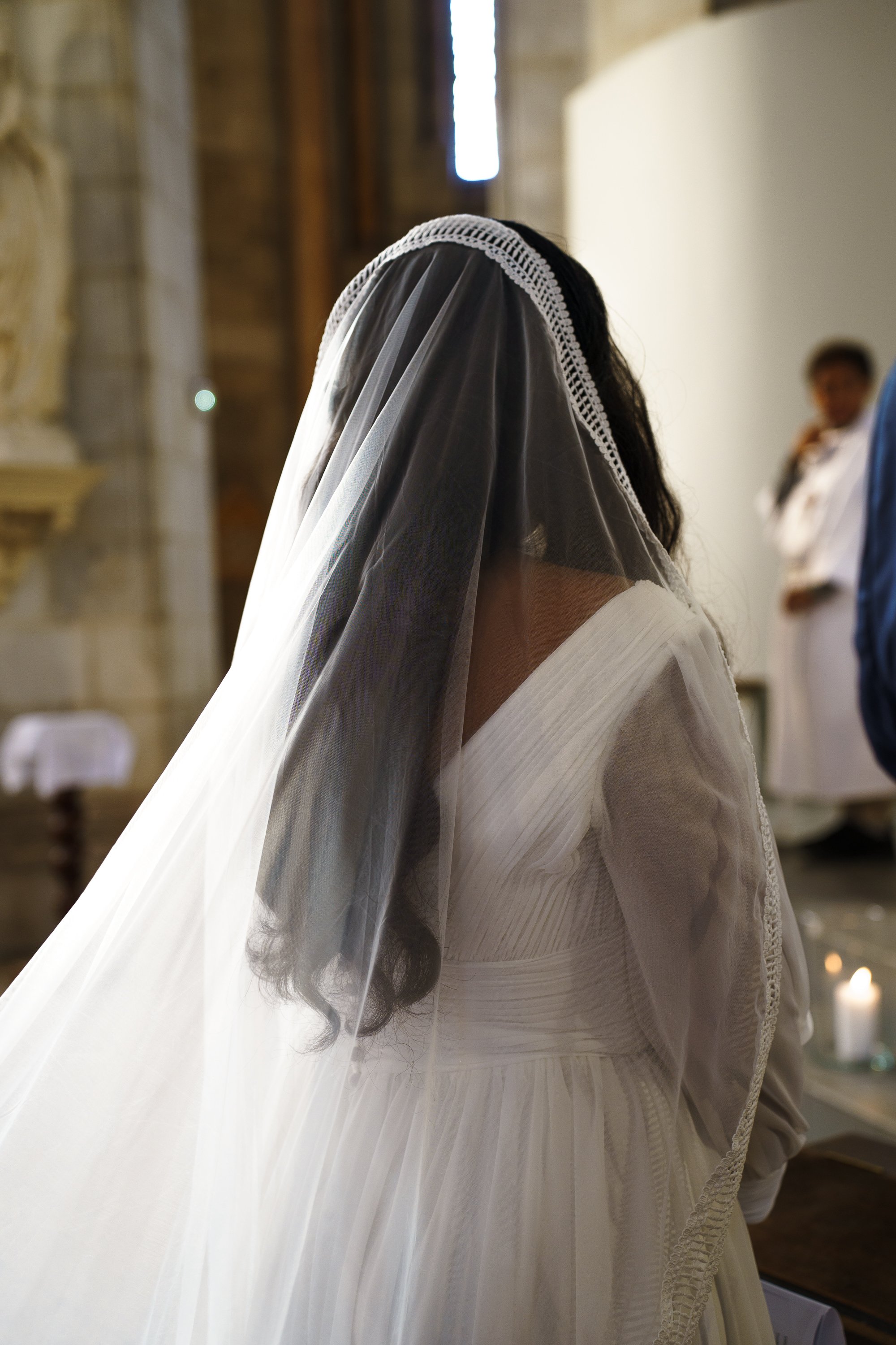 Une femme portant une robe blanche de mariage sous un voile transparents dans une église, lors d'une cérémonie.
