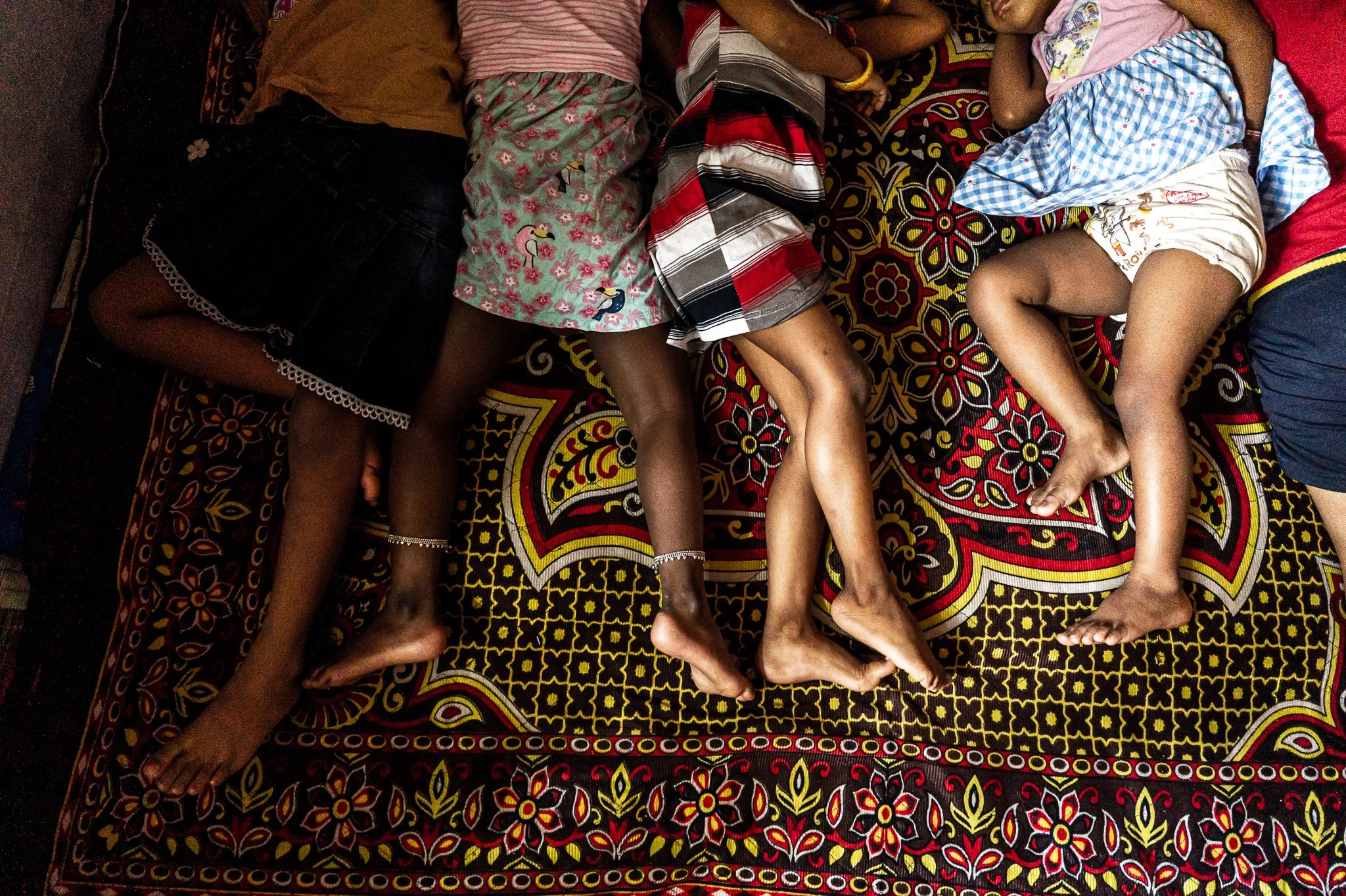 Plusieurs enfants allongés sur un tapis coloré, montrant uniquement leurs jambes.