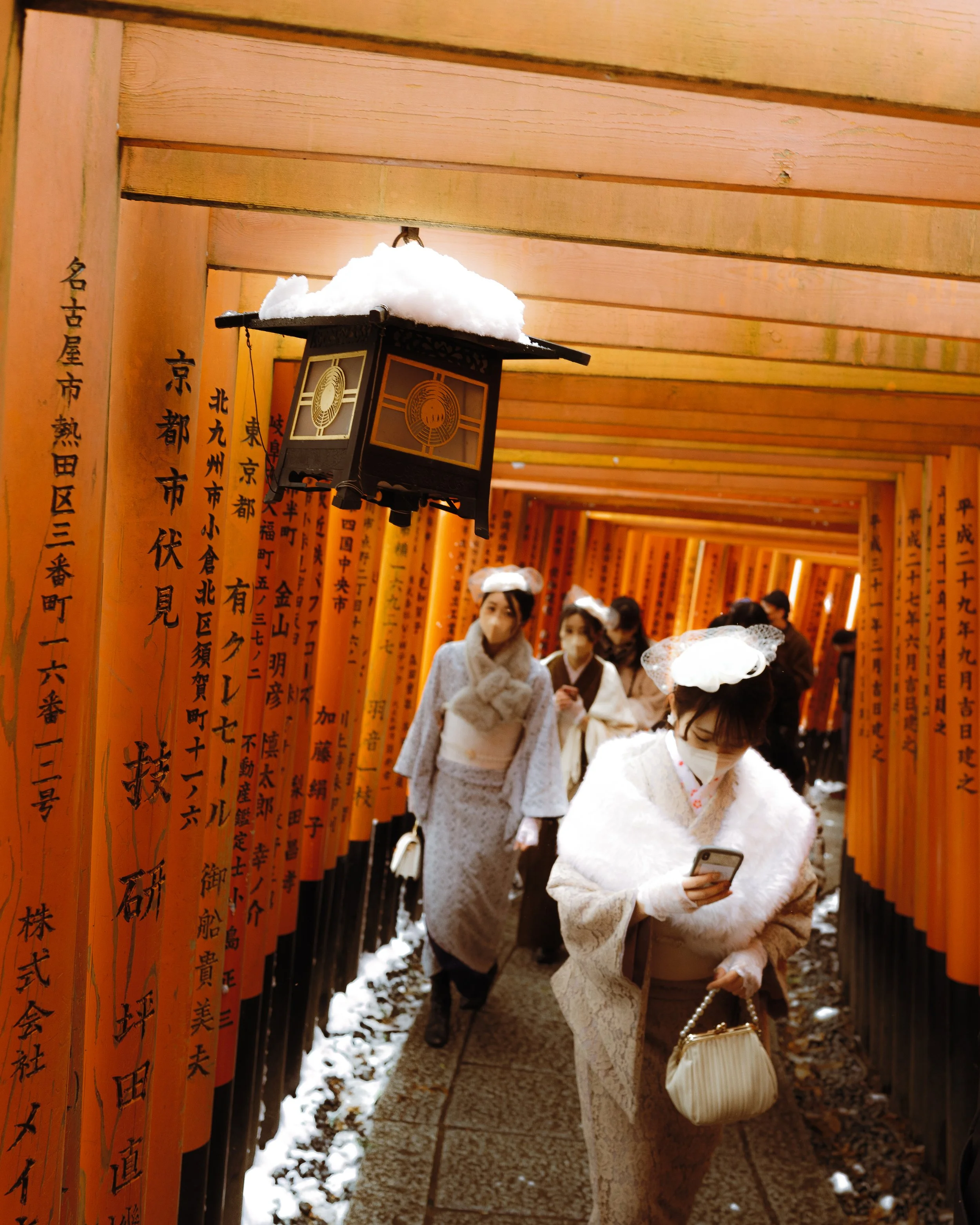 Des personnes en kimono marchent sous des torii rouges dans un sanctuaire japonais enneigé.