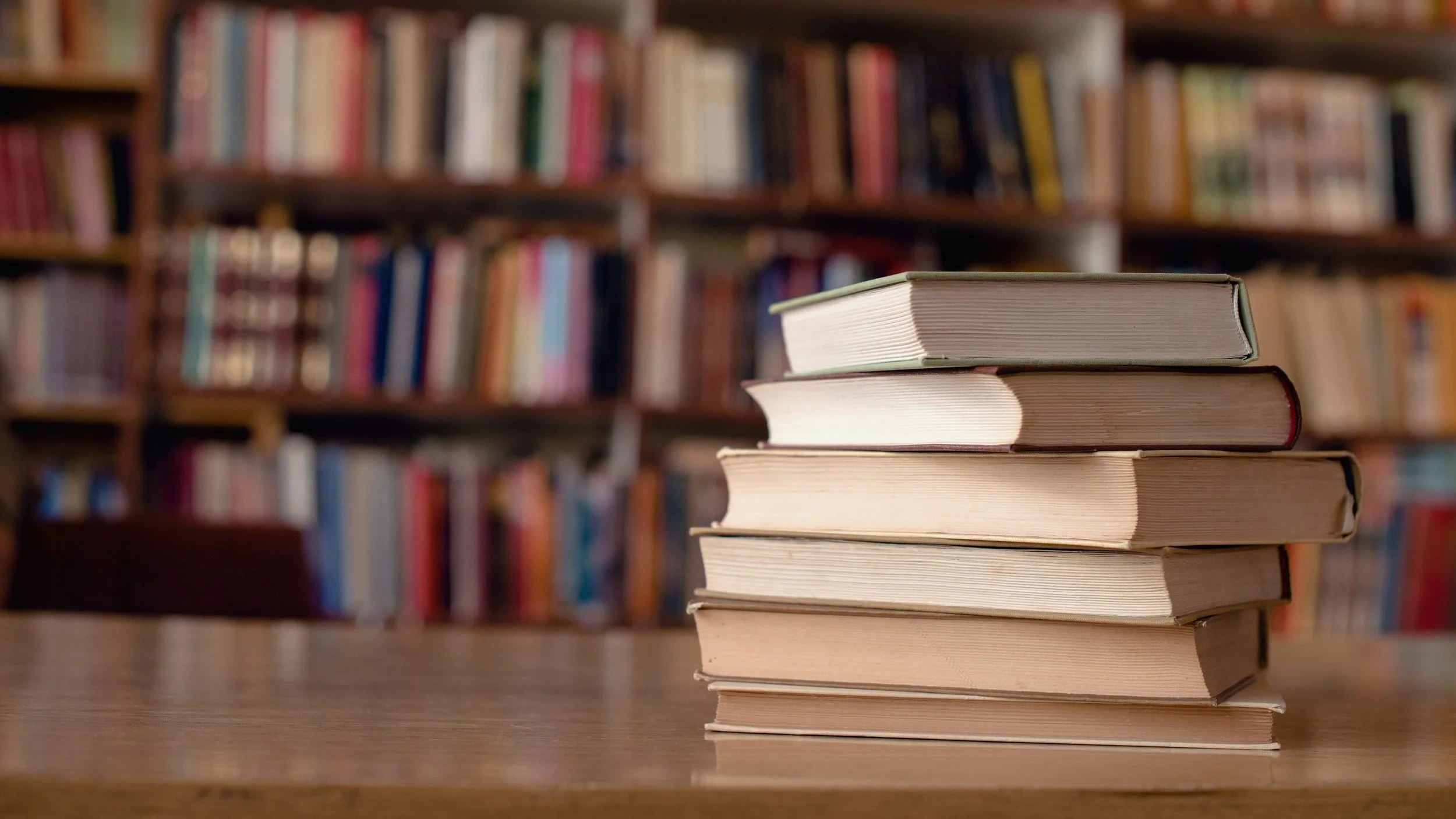 Stack of twelve books with various titles and authors, arranged on a wooden surface.