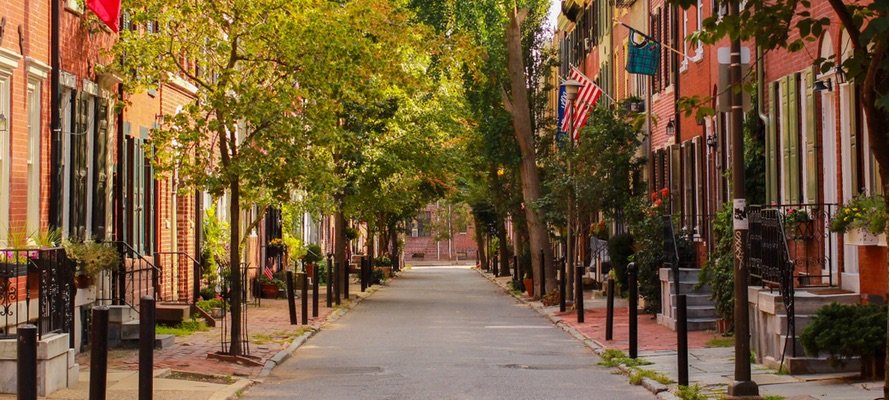 Quiet street lined with brick townhouses, trees, and American flags on a sunny day