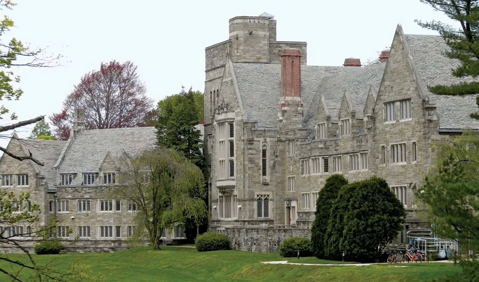 A large stone Gothic-style building with pointed roofs, tall windows, and a central tower, surrounded by green trees and grass.