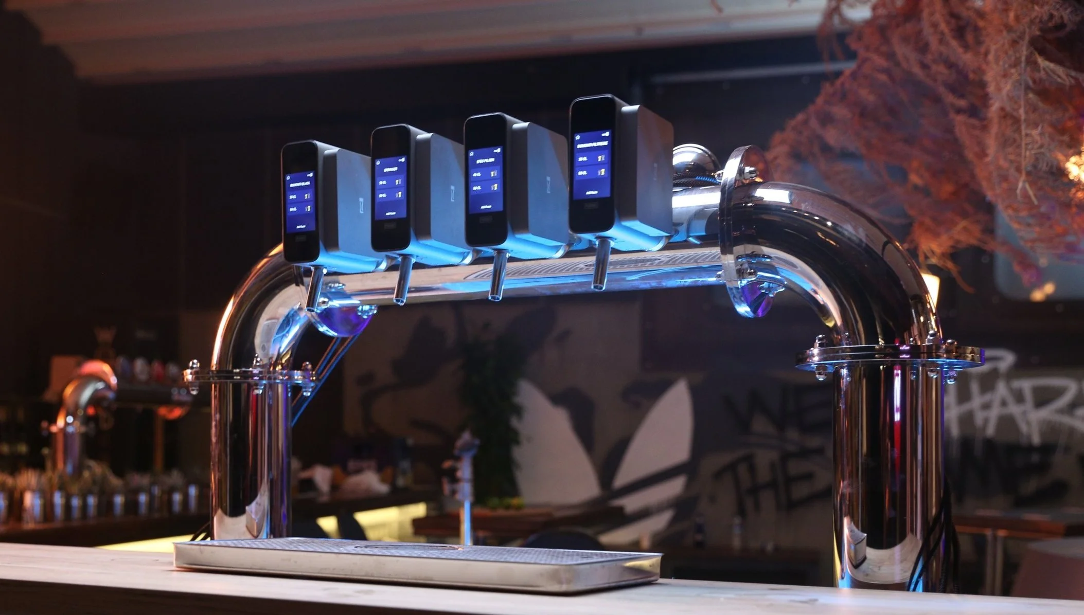 A tap with six digital devices mounted on it, displaying various information on their screens, in a dimly lit bar or restaurant setting.