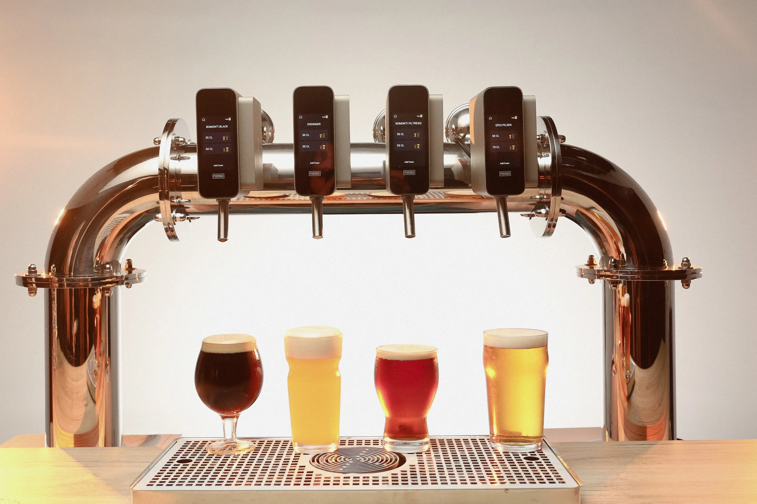 A beer dispenser with four taps pouring different types of beer into glasses on a wooden surface.