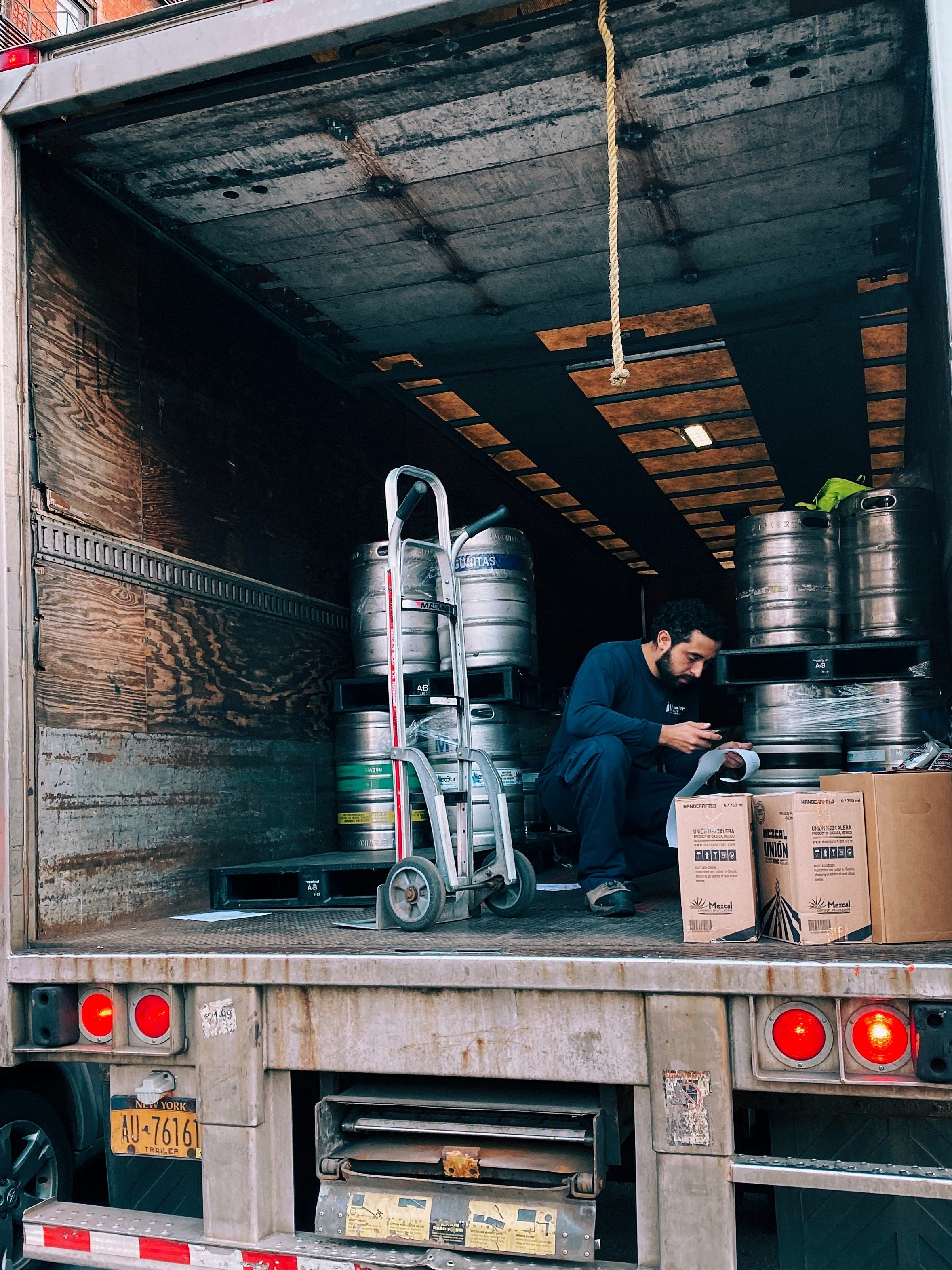 A man sitting inside an open truck with beer kegs, boxes, and a hand truck, possibly preparing or organizing deliveries.