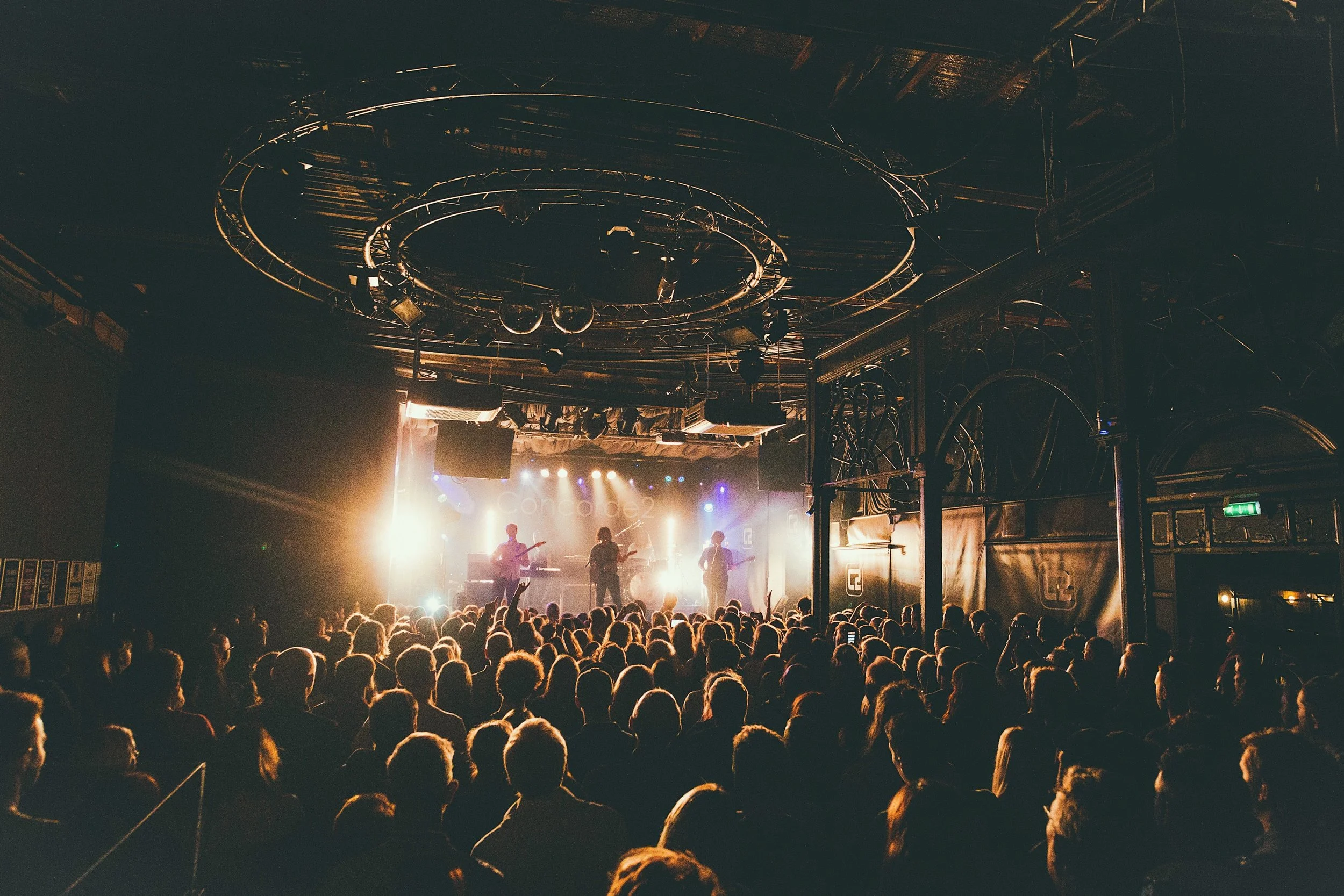 A crowd watching a live band performance on stage at a concert venue with bright lights and a dark interior.
