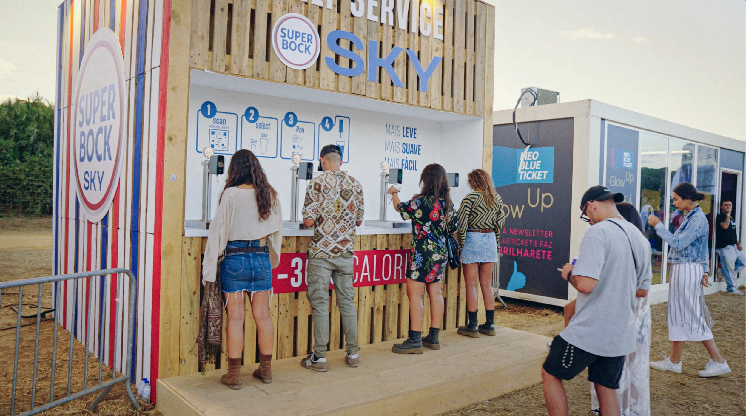 People lined up at a ticket booth for the Sky event, located outdoors, with a wooden structure and banners indicating ticket purchasing instructions.