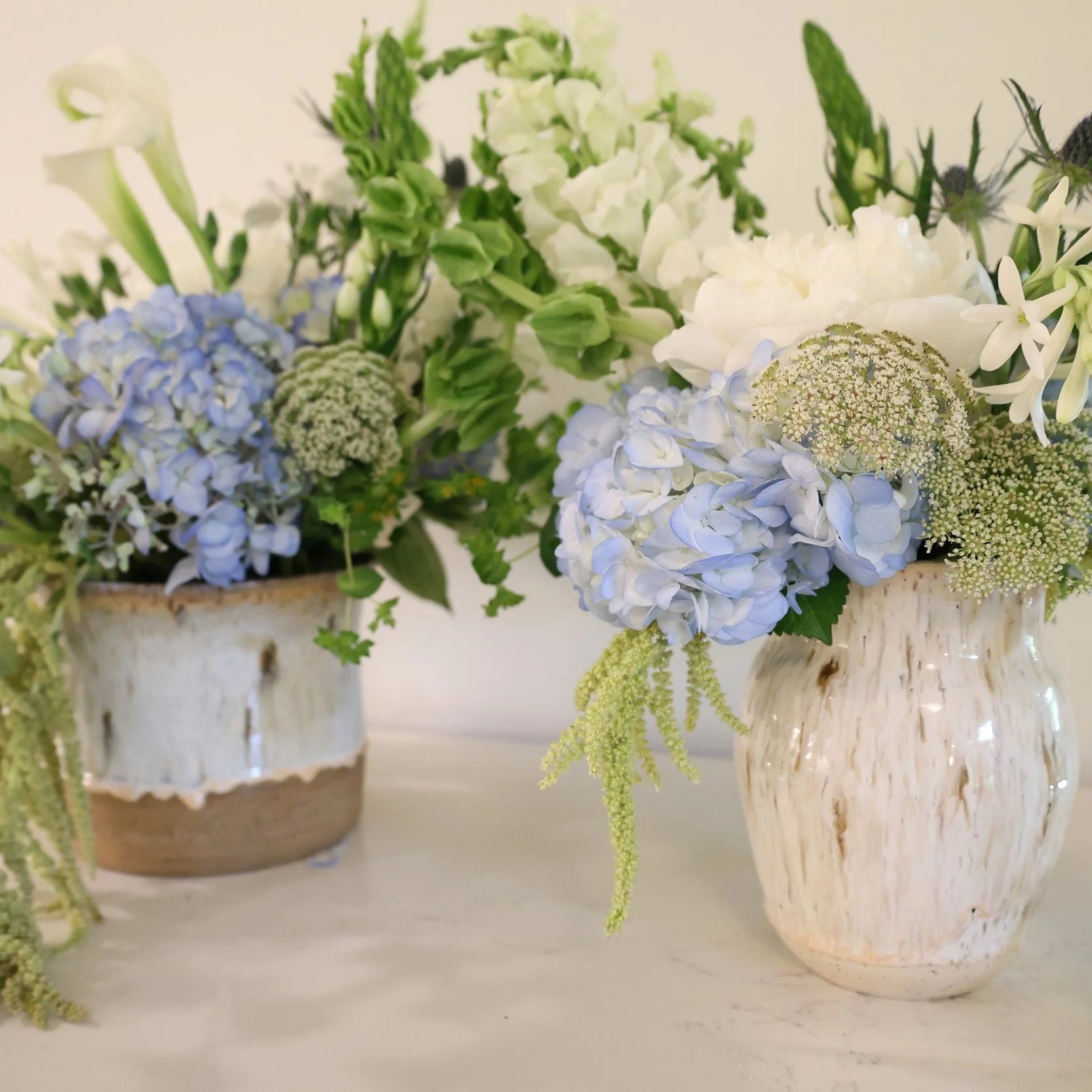 Bouquet of white and light blue flowers in a rustic ceramic vase.