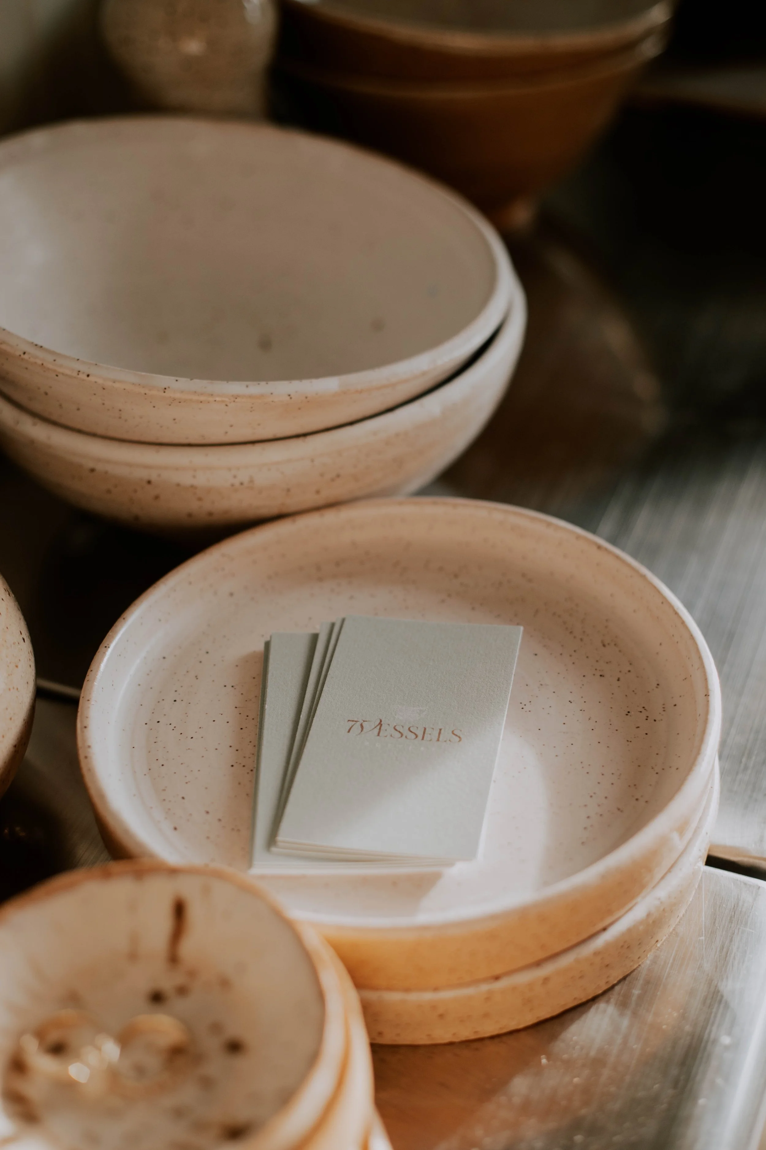 Close-up of beige speckled bowls stacked together, with a star-shaped notepad or paper inside one of the bowls that has the word 'TASSELS' written on it.