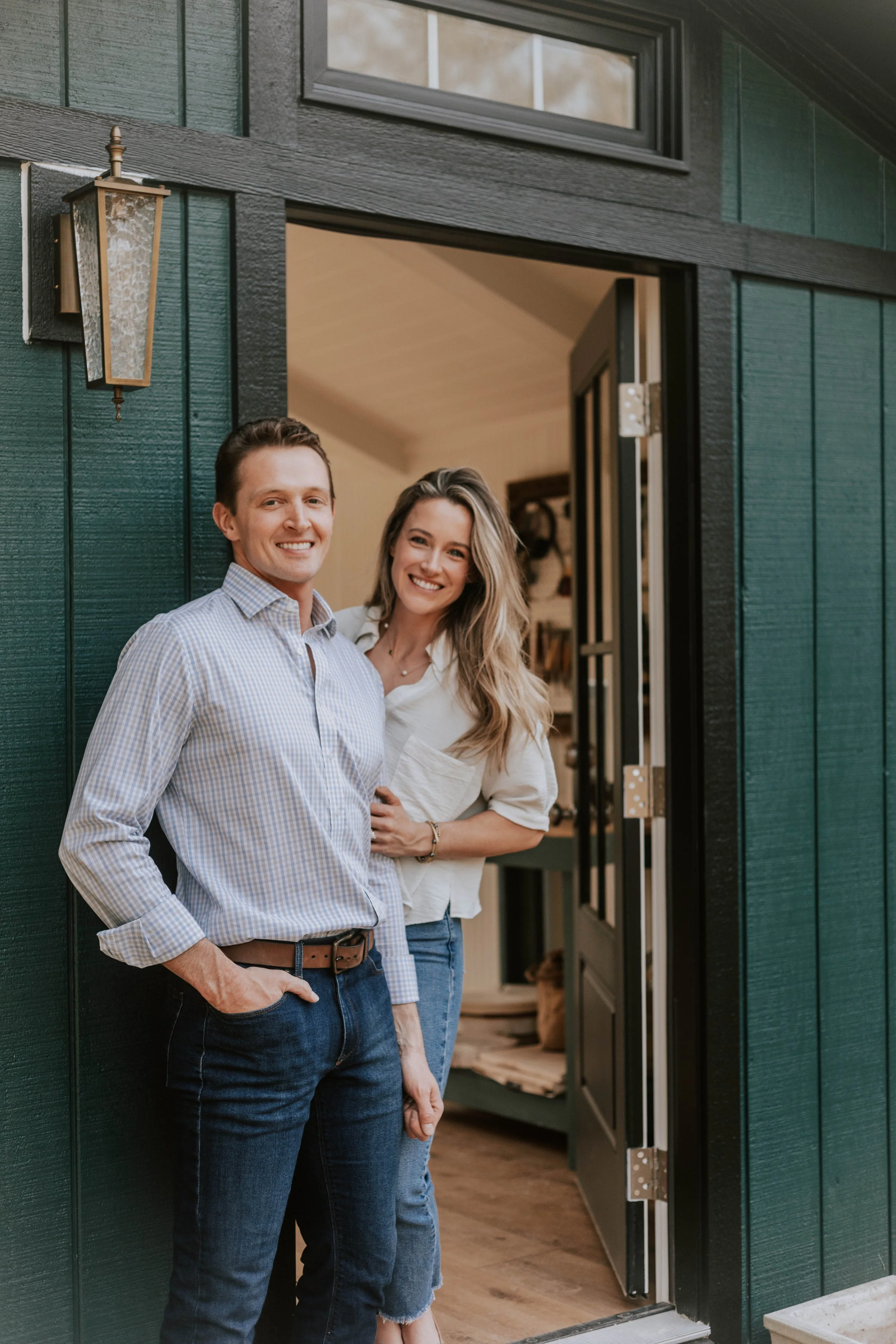 A smiling man and woman standing at the open door of a house, looking outside.