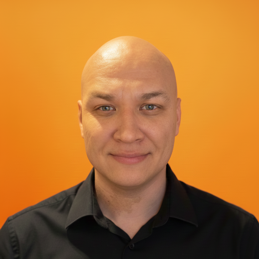 Porträt eines Mannes vor einem orangefarbenen Hintergrund, lächelnd, mit schwarzem Hemd.