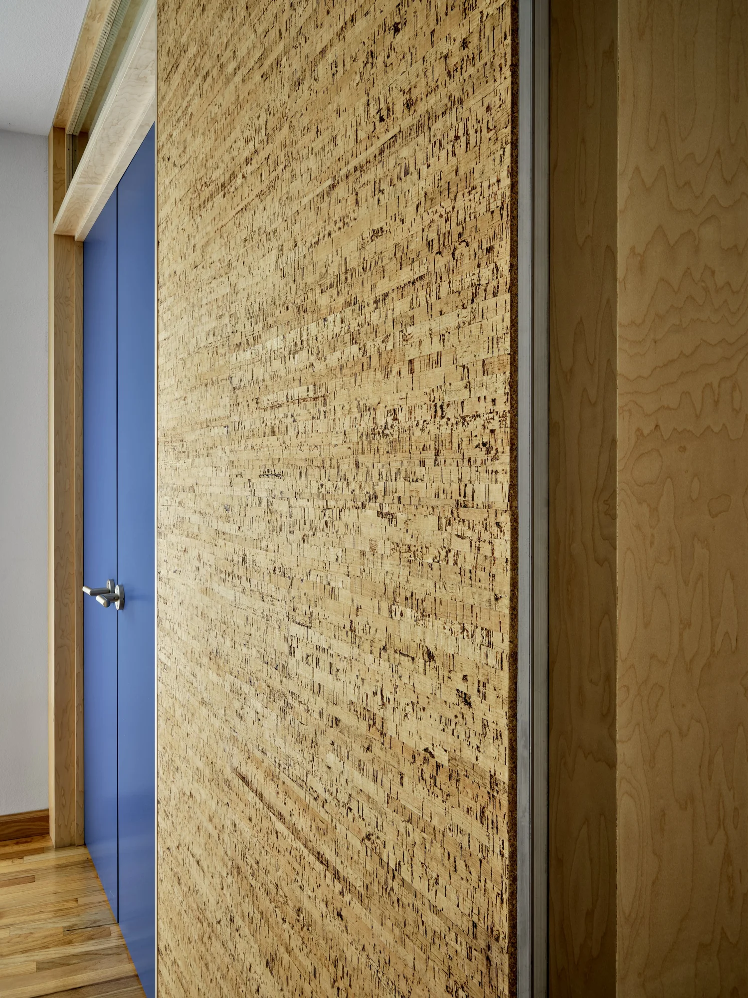 Close-up of cork wall and blue door detail at Three Cork Walls, showing layered textures and material junctions.
