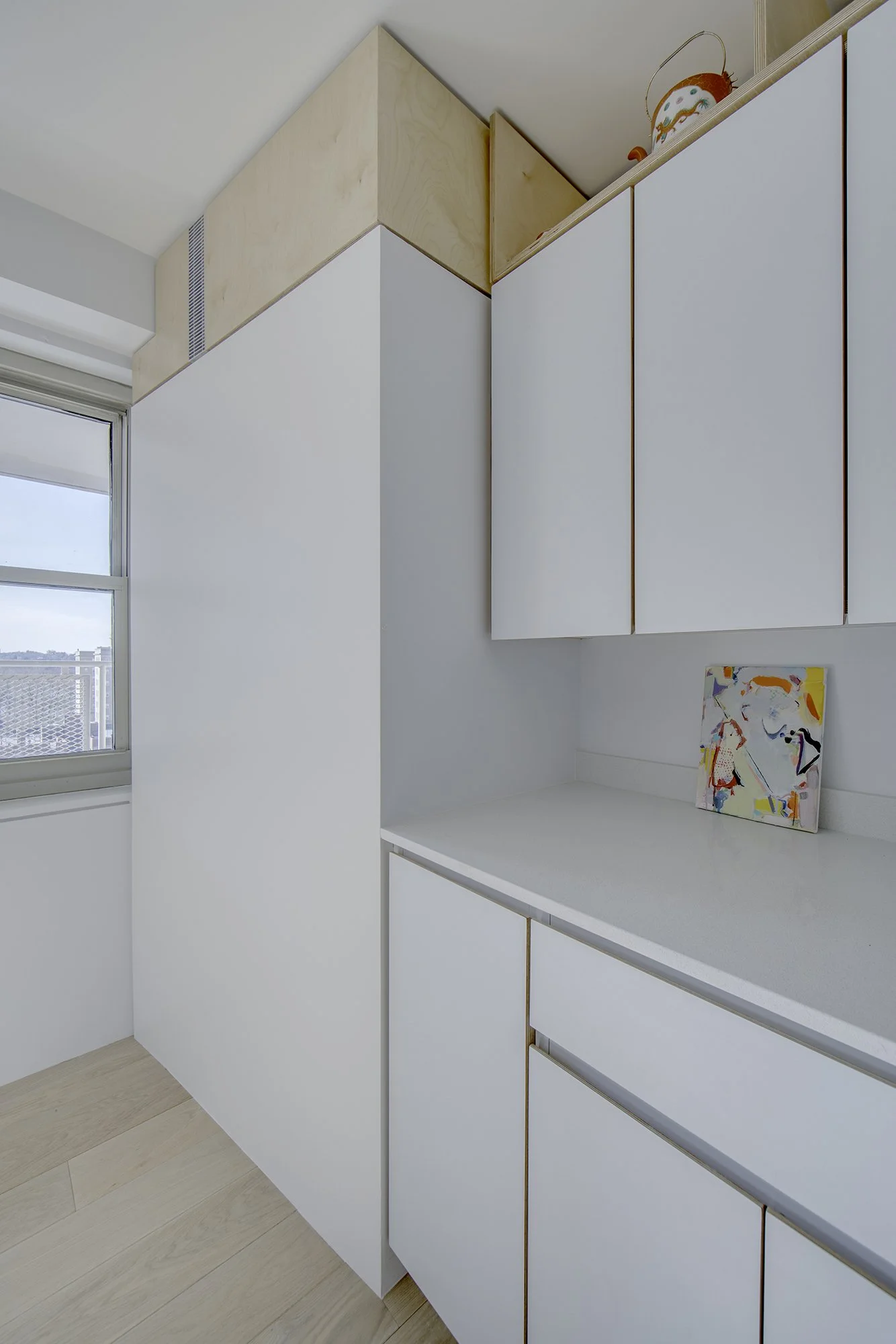 Custom cabinetry detail in Harlem Studio showing white cabinets with concealed handles and wood trim, paired with overhead storage compartments.