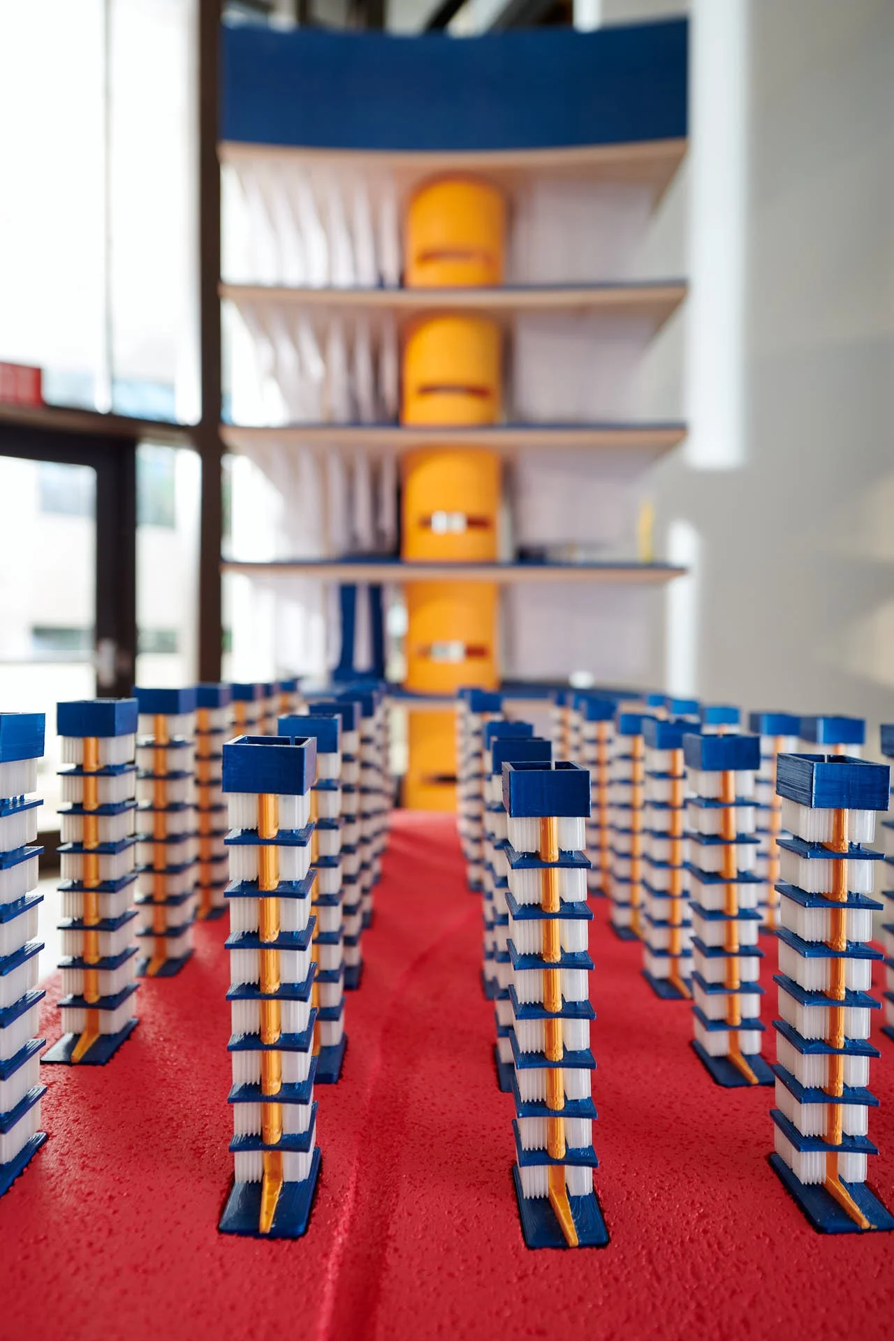 Close-up view of The Great Lakes Architectural Expedition installation featuring rows of blue and white column models arranged on a red surface.