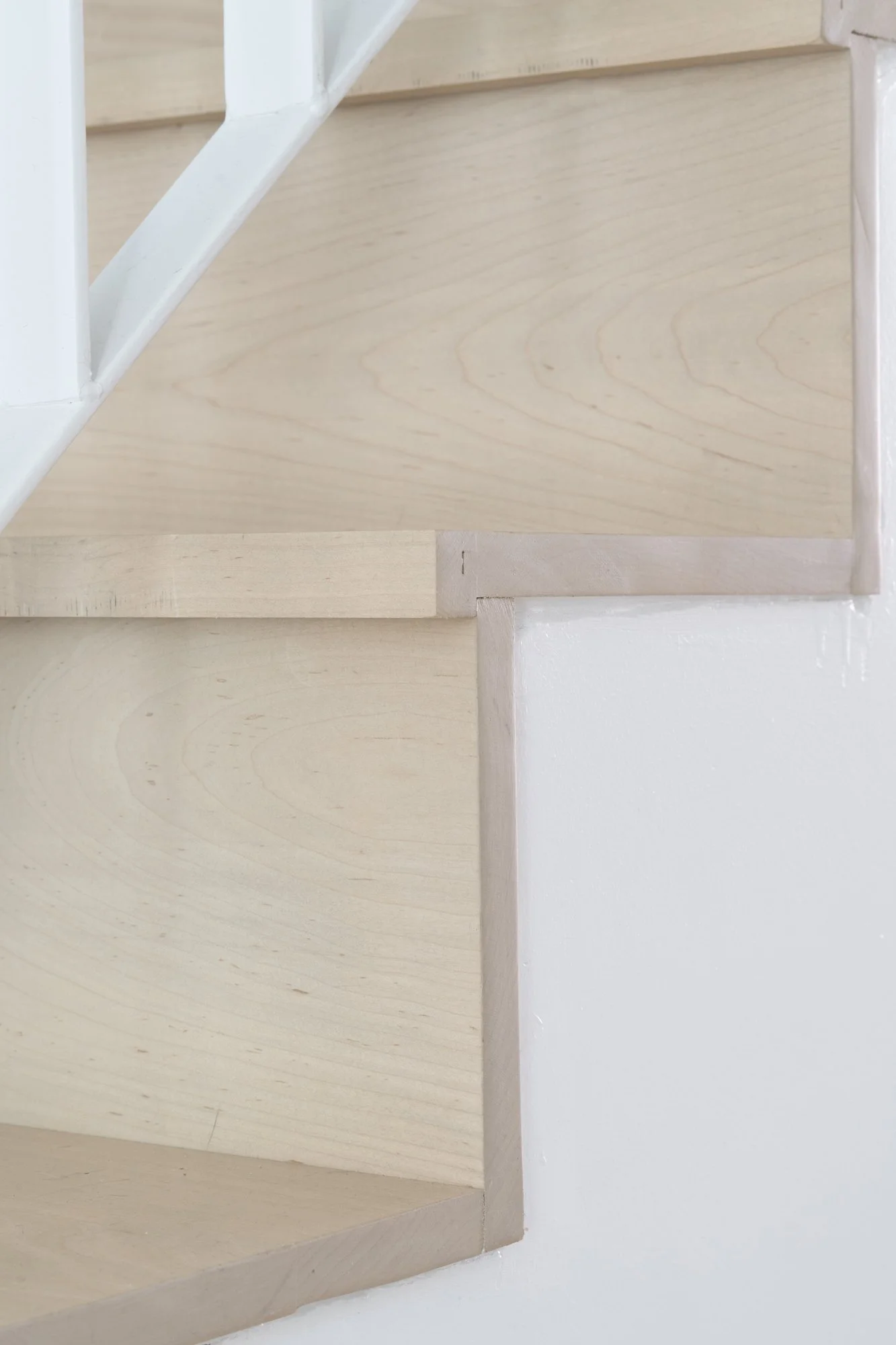 Detail of Narrow Townhouse staircase showing light wood treads, white risers, and trim connection at railing base.