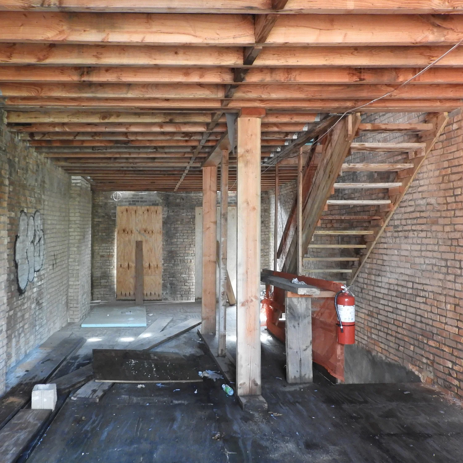 Interior view of Narrow Townhouse during construction, showing exposed brick walls, floor joists, and temporary wood stair framing.
