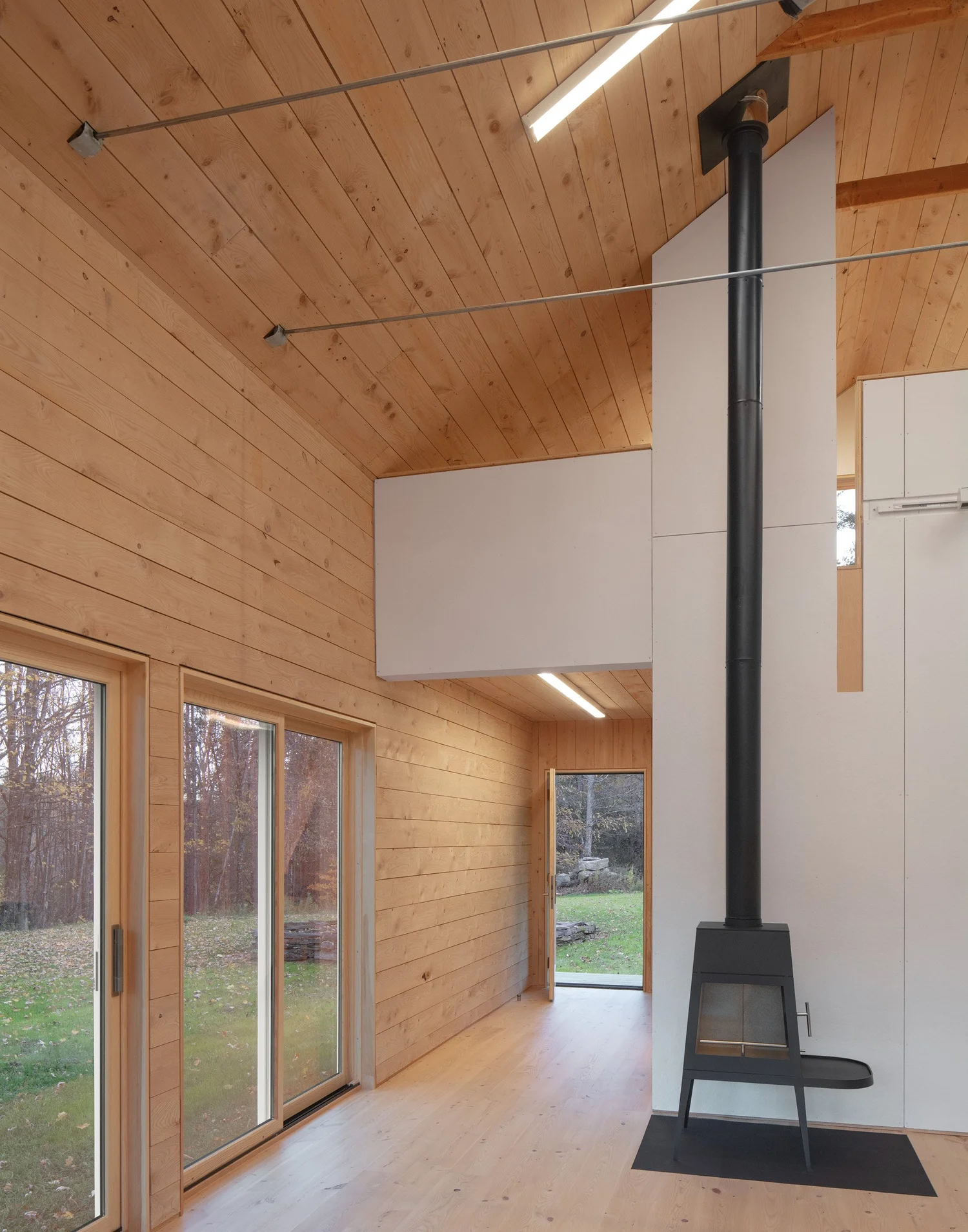 Barnard Barn living space with tall black wood stove extending to the ceiling, sliding glass doors, and wood-paneled walls.