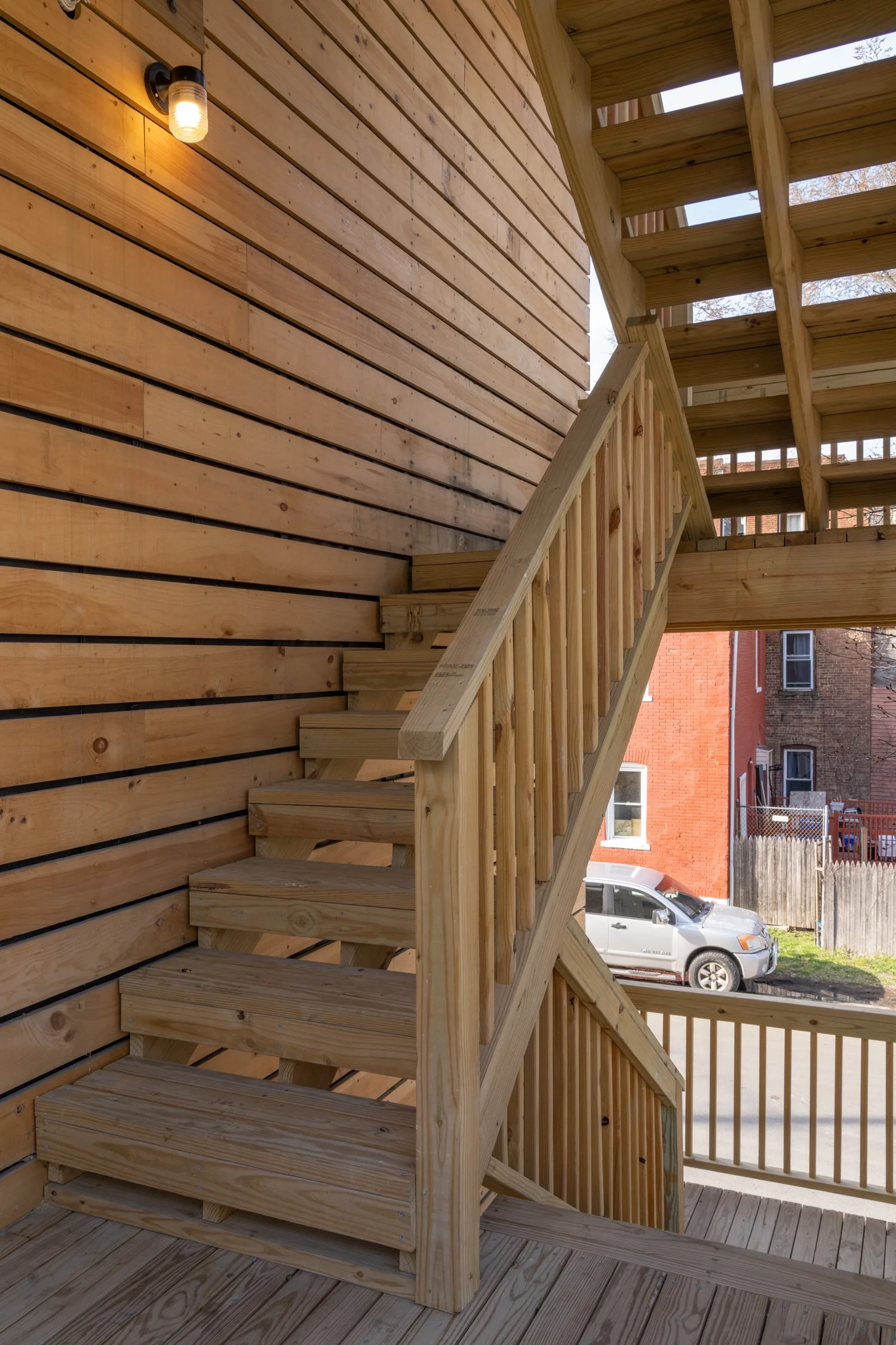 Exterior stair landing at Swift Street Residences with wood cladding, railing, and natural light from an exposed bulb fixture.