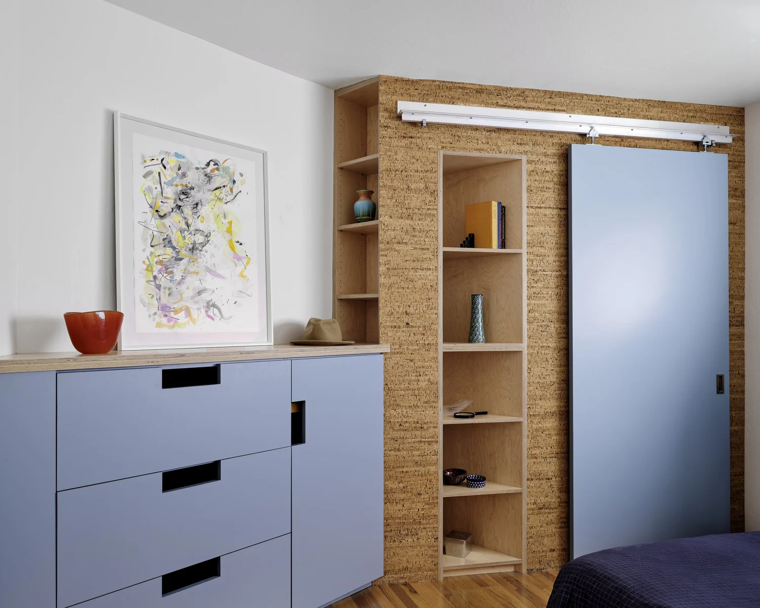 Interior of Three Cork Walls bedroom with built-in cork wall shelving, a light blue sliding door, and matching blue cabinetry with recessed pulls.