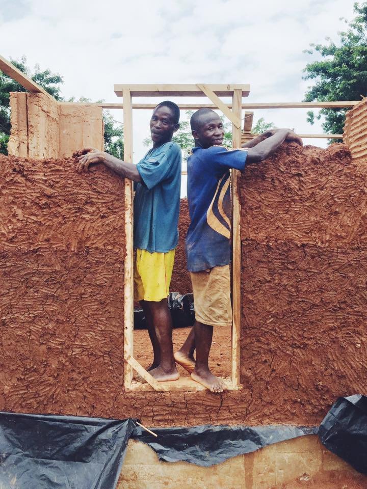 Two craftsmen building cob walls around a window opening in the Mudhouse.